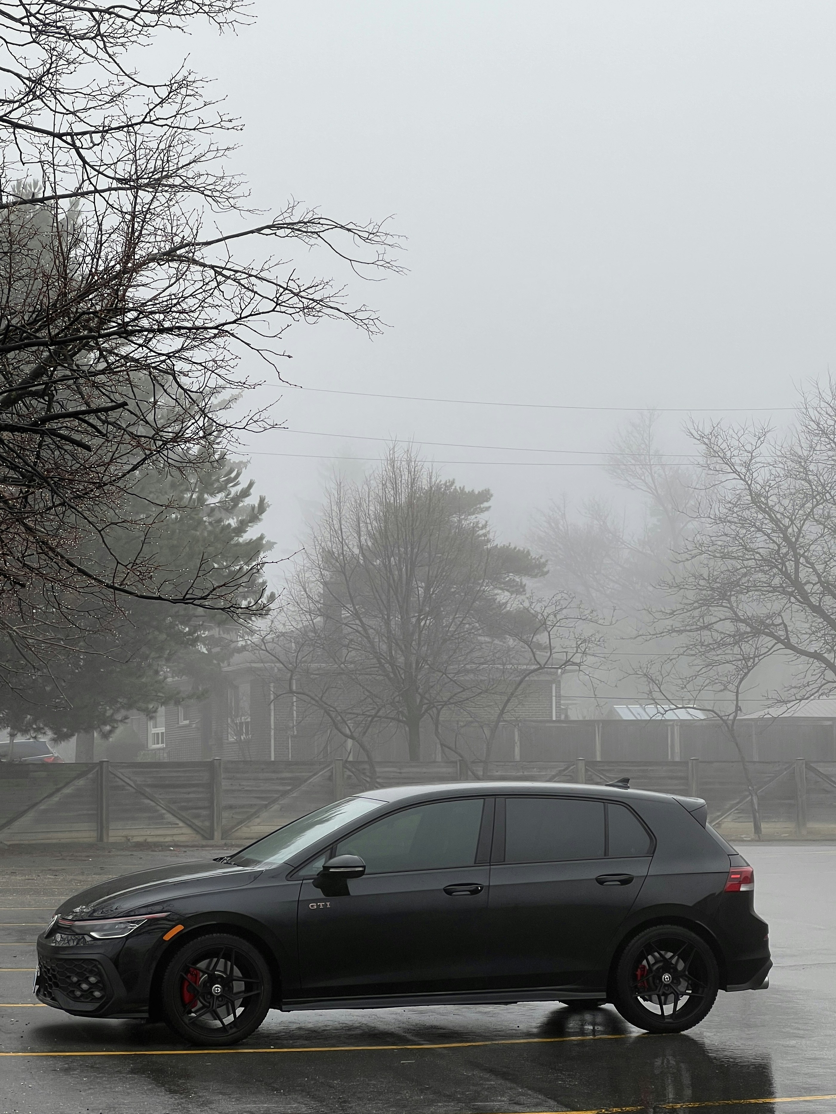 Dark gray car parked in a foggy, wet outdoor lot.