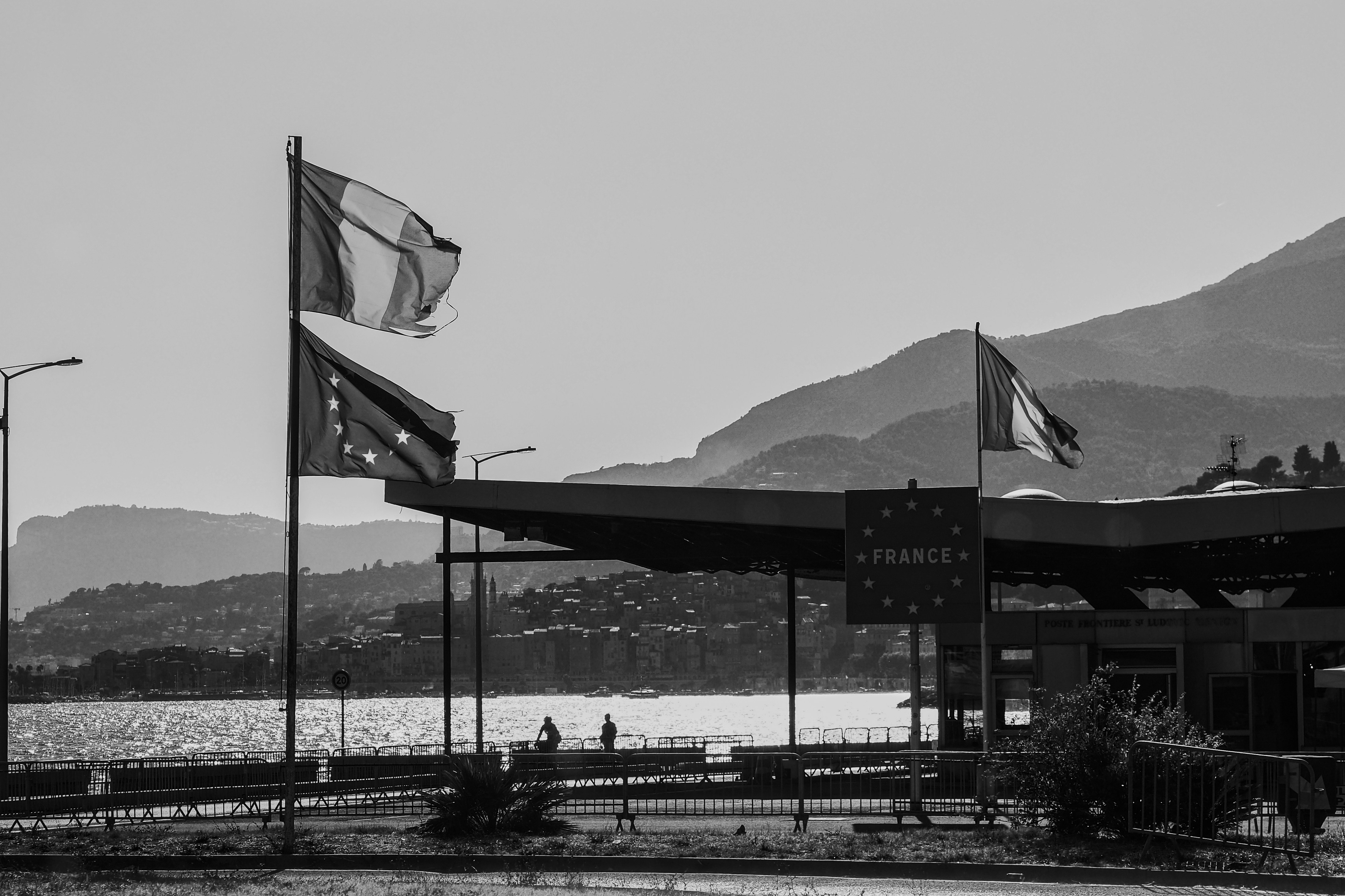 Border crossing with french and eu flags near mountains.