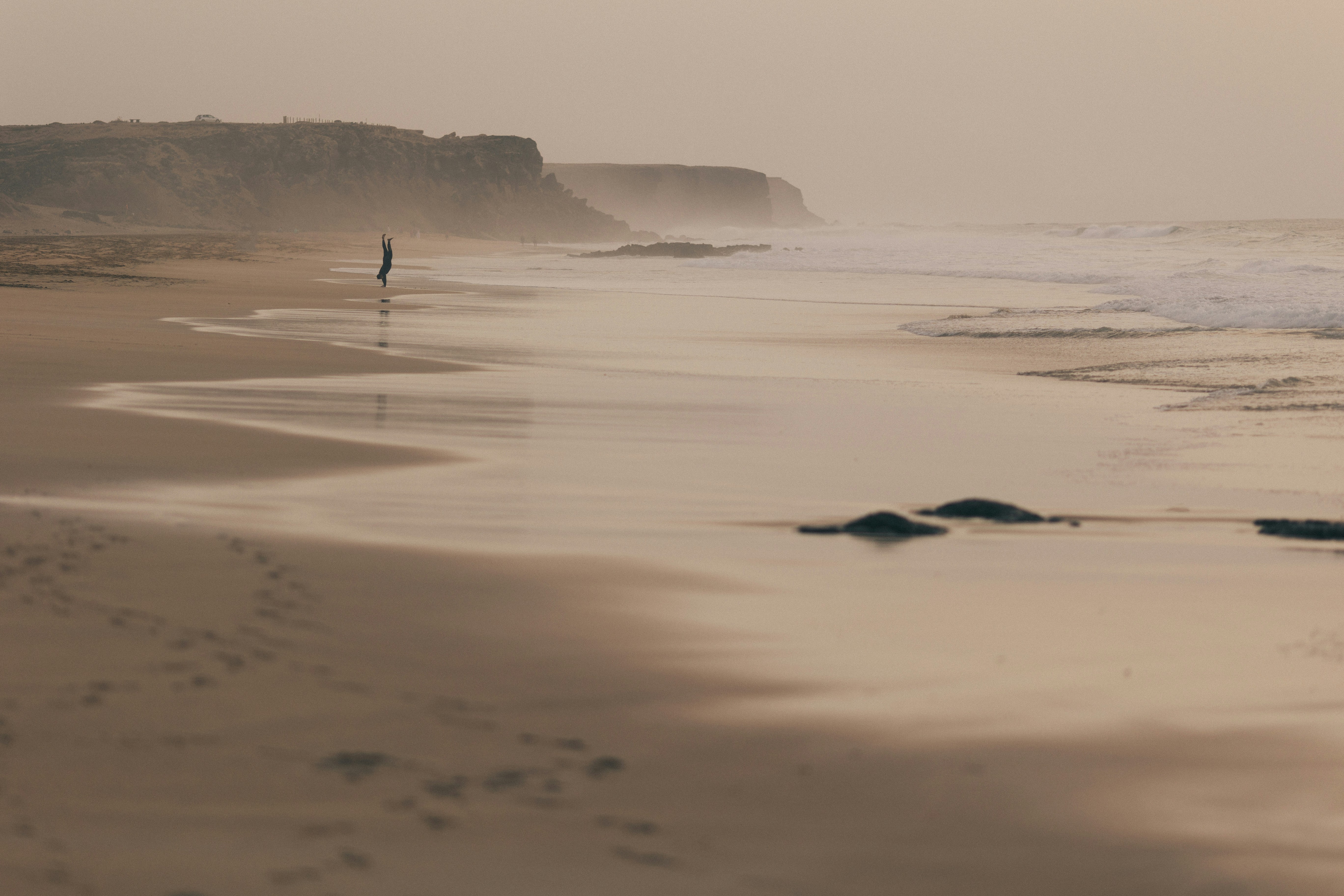 Serene misty beach with a lone figure walking near cliffs.