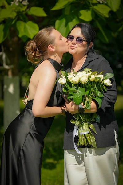Young woman kisses older woman holding white roses