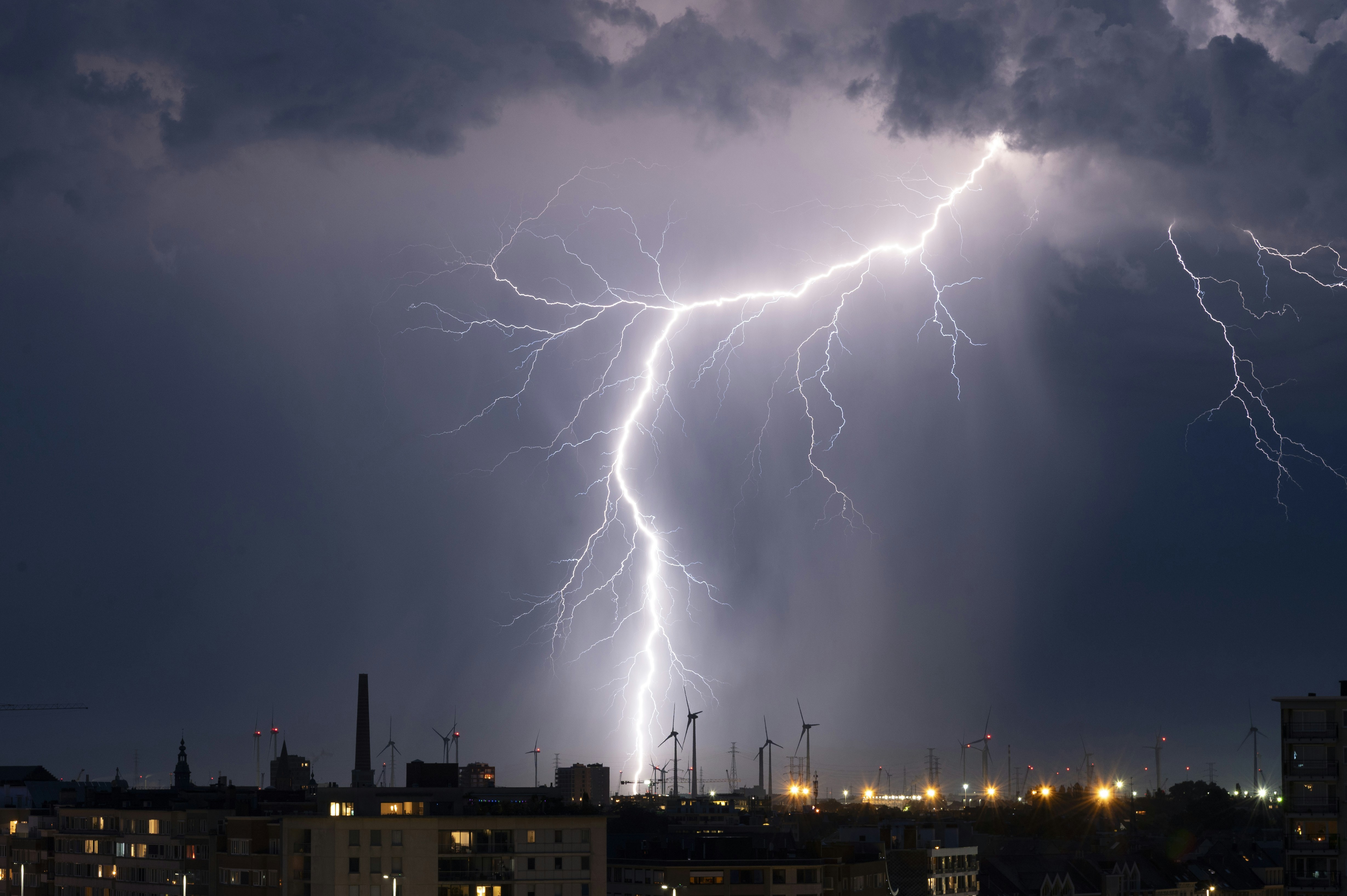 Powerful lightning bolt strikes city skyline at night.
