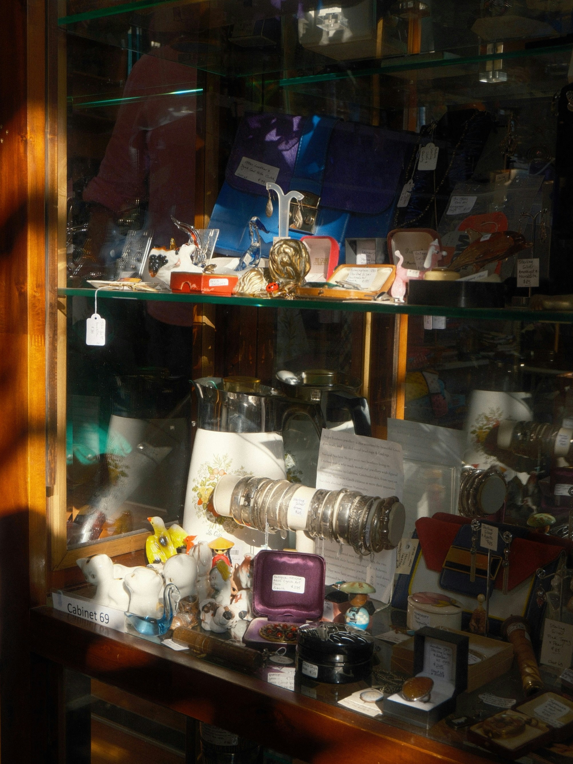 Assorted items and jewelry displayed in a sunlit glass cabinet.