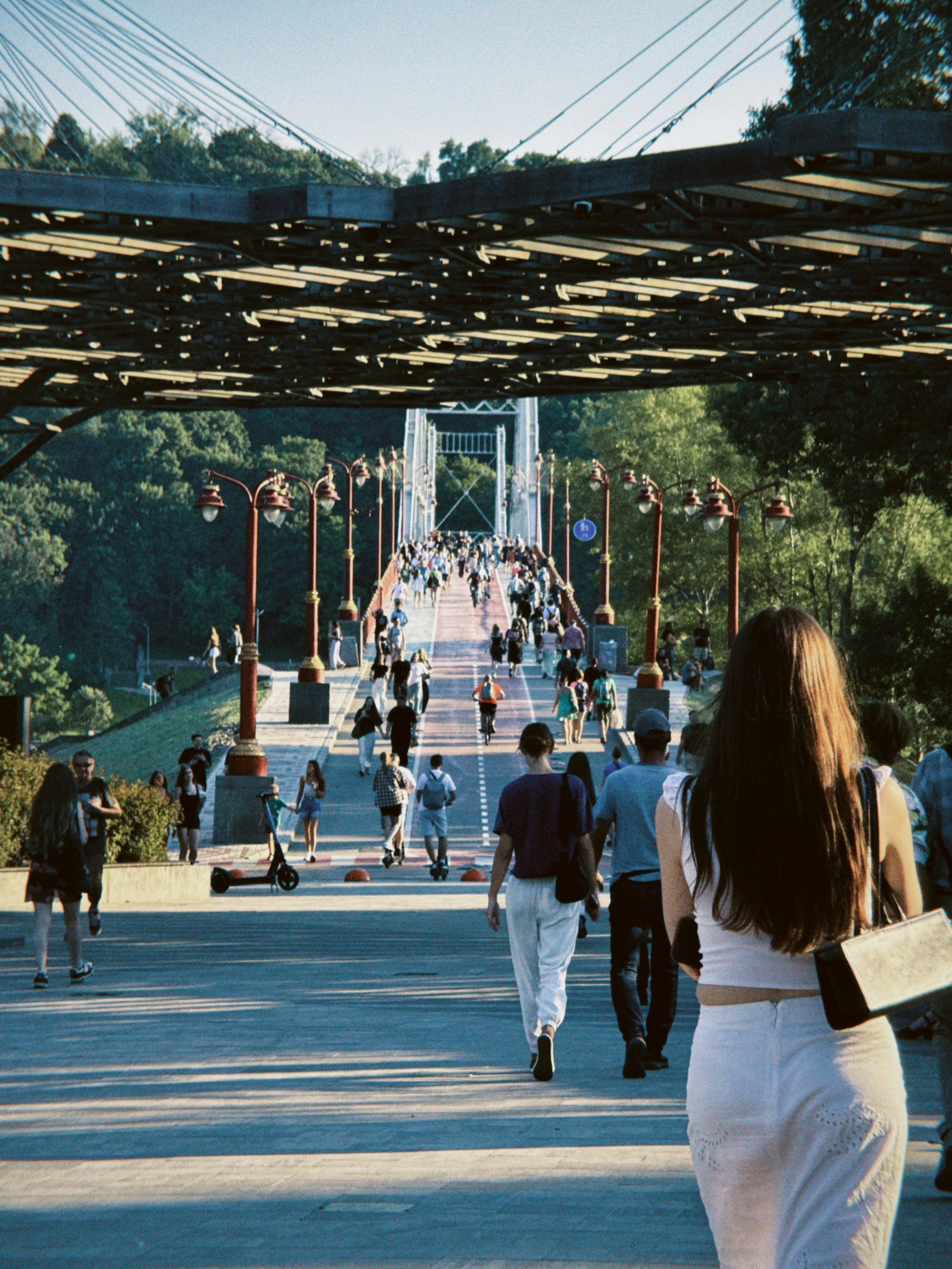 Crowds of people stroll along a large suspension bridge.