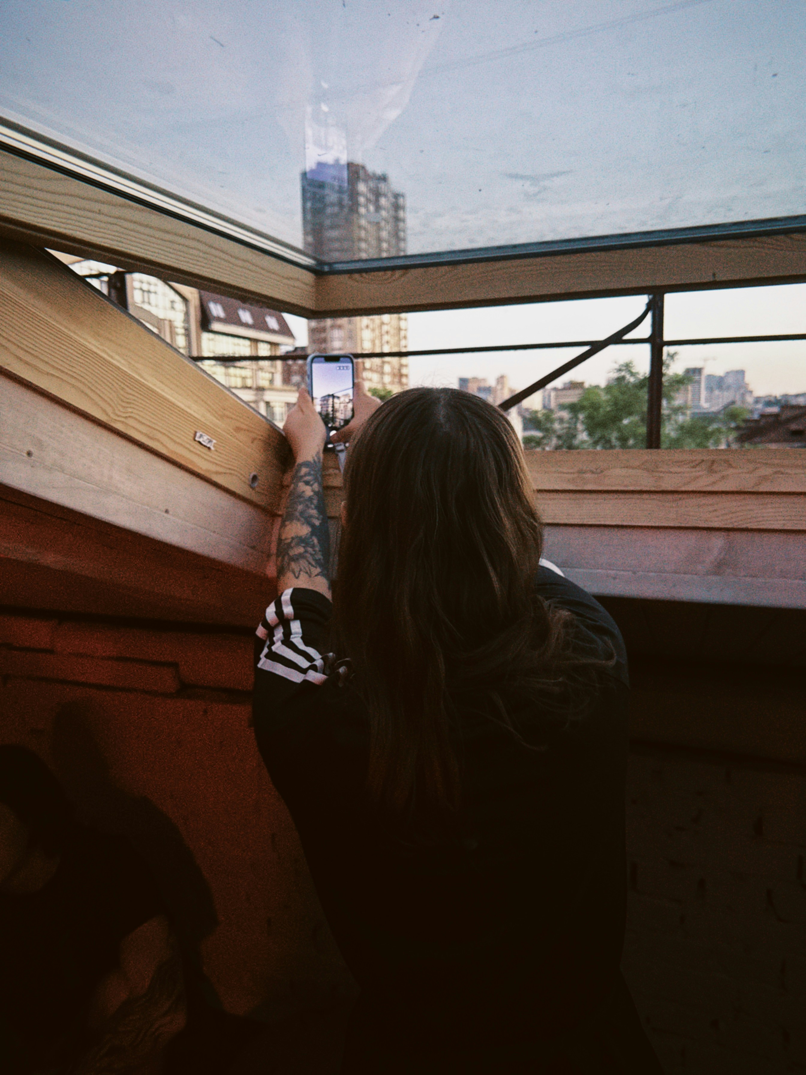 Long-haired person capturing city view with a smartphone.