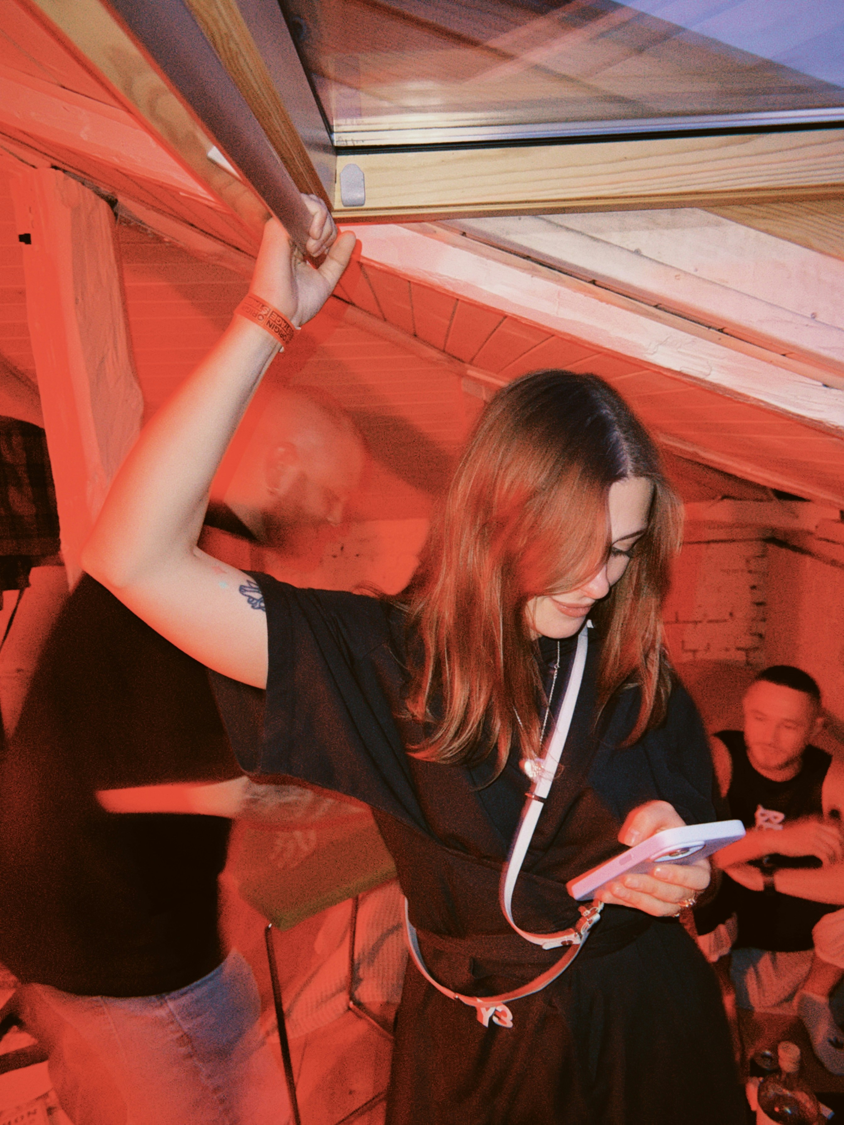 Young woman smiling and using phone in red-lit room.