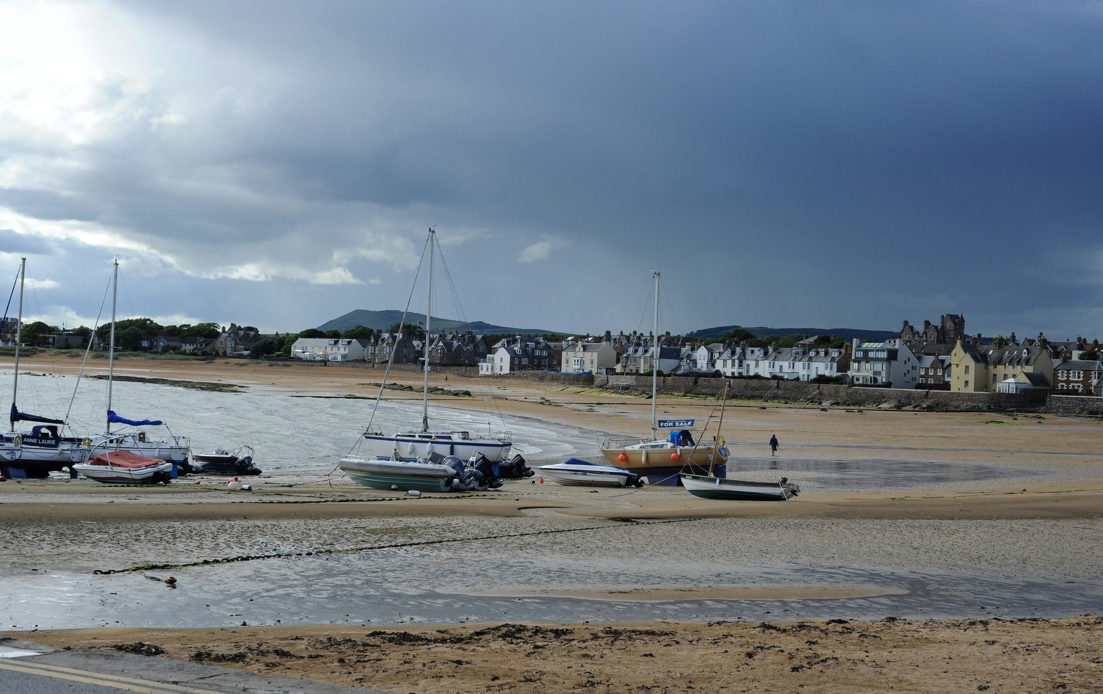 Boats on sandy beach with town and dark, cloudy sky
