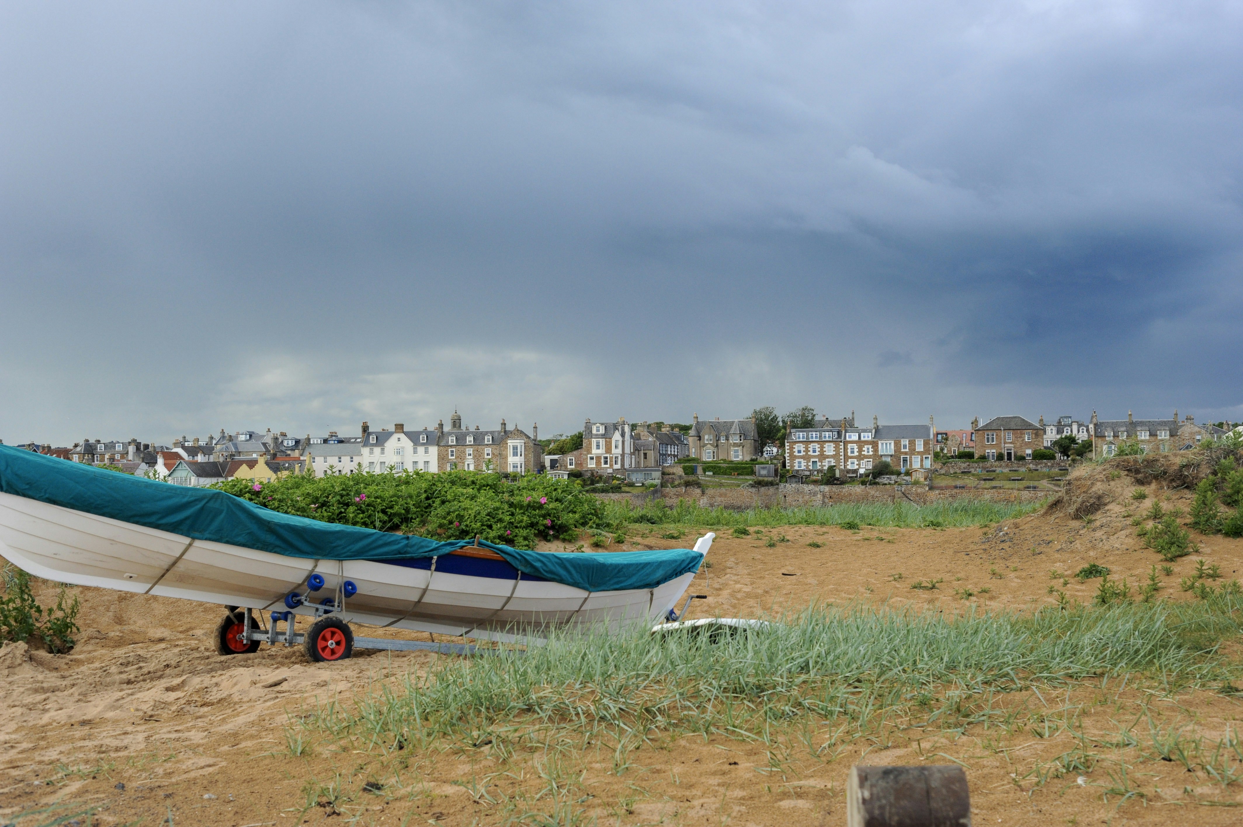 Covered boat on sandy beach with town under stormy sky