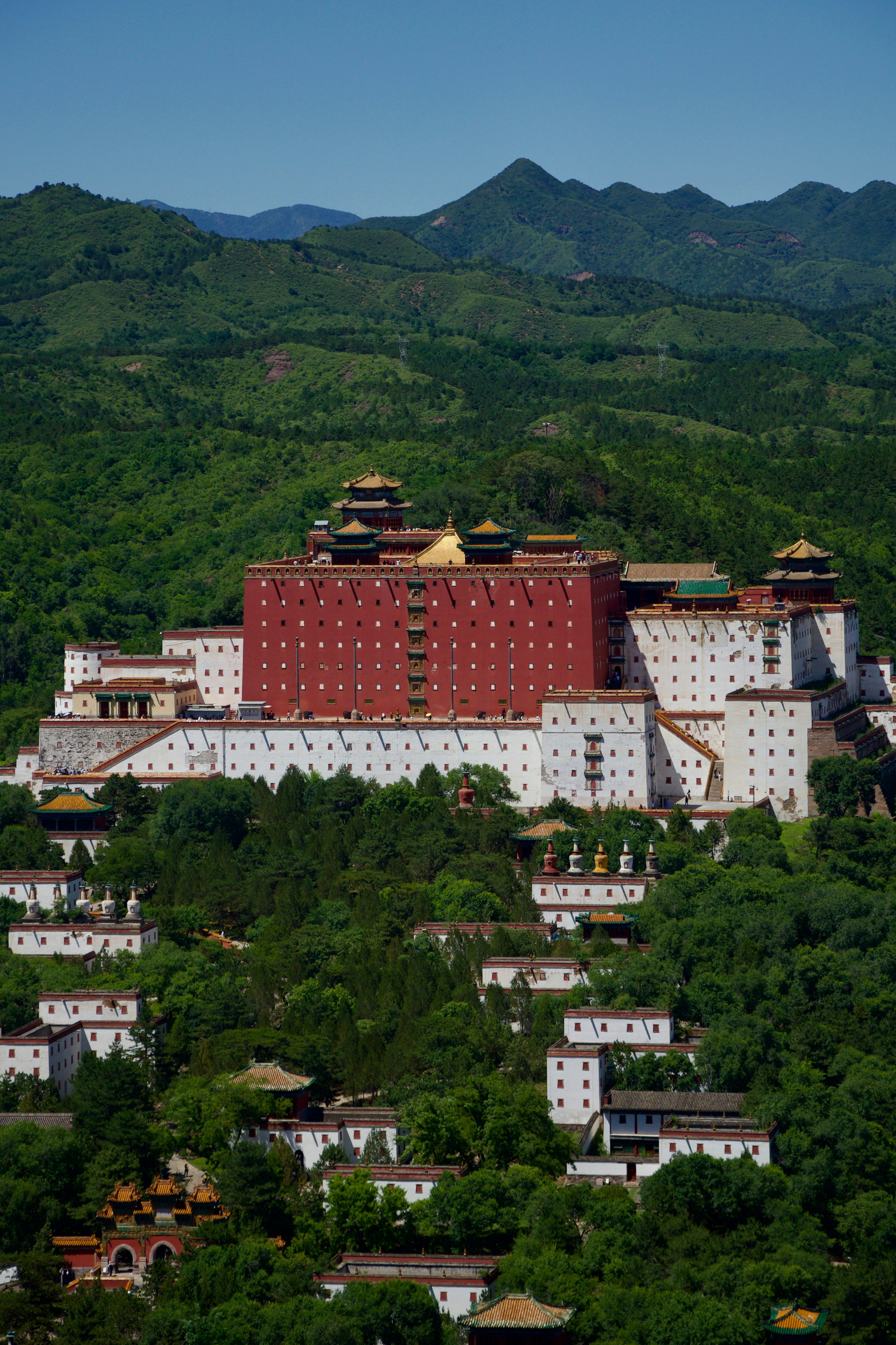 A large red and white palace complex in green mountains