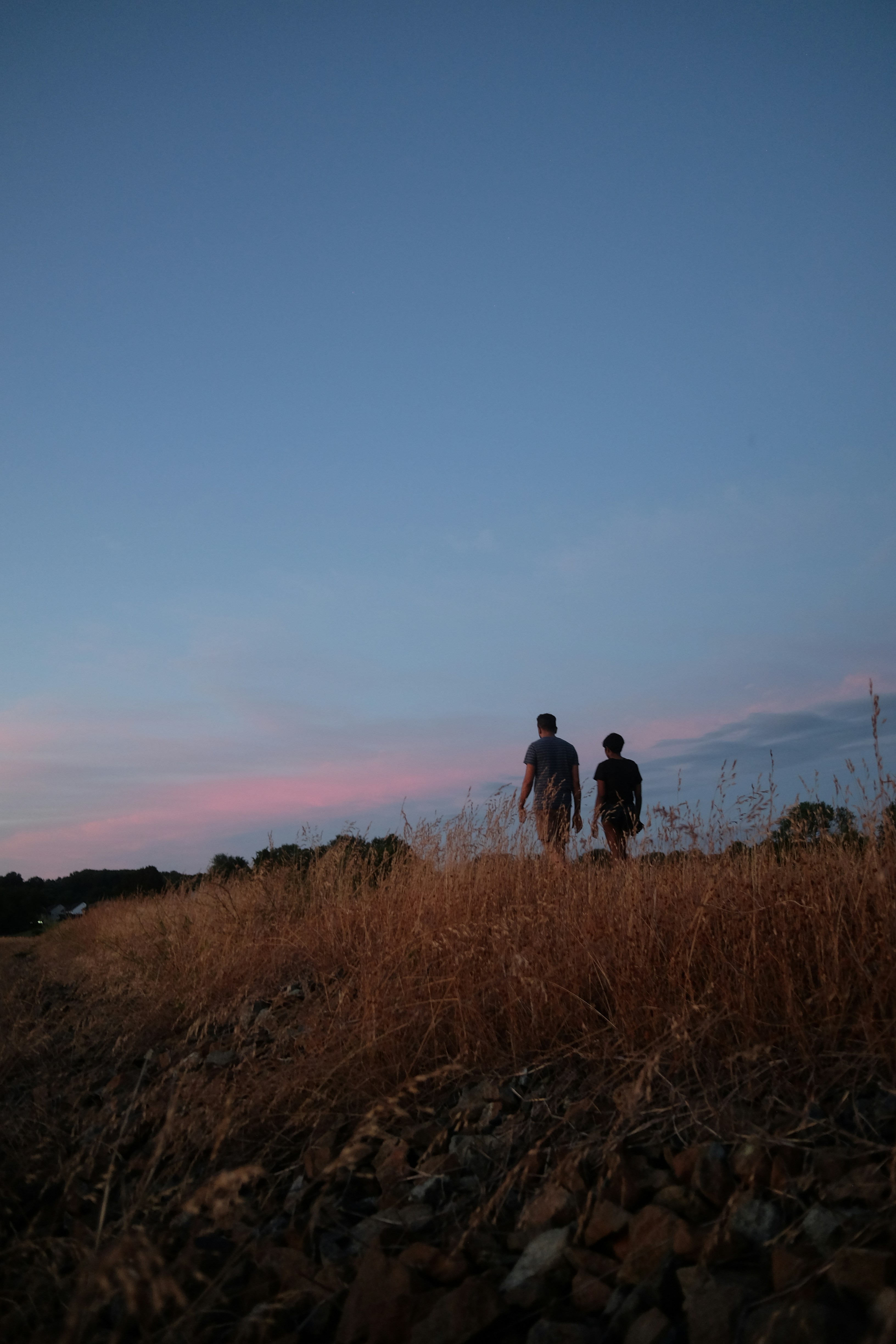 Two people walk on a dry field at sunset.