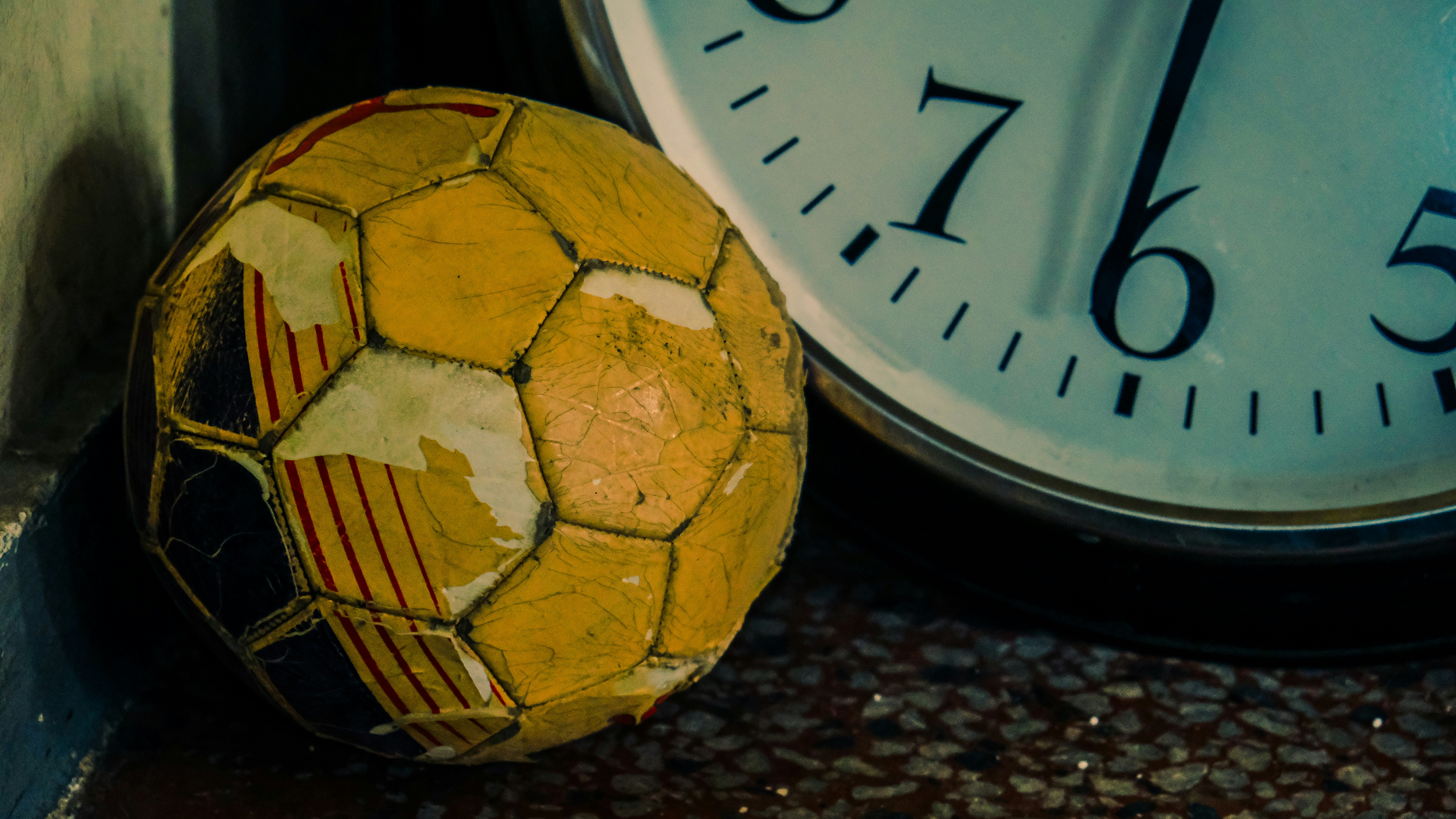 An old, worn yellow soccer ball rests beside a clock.