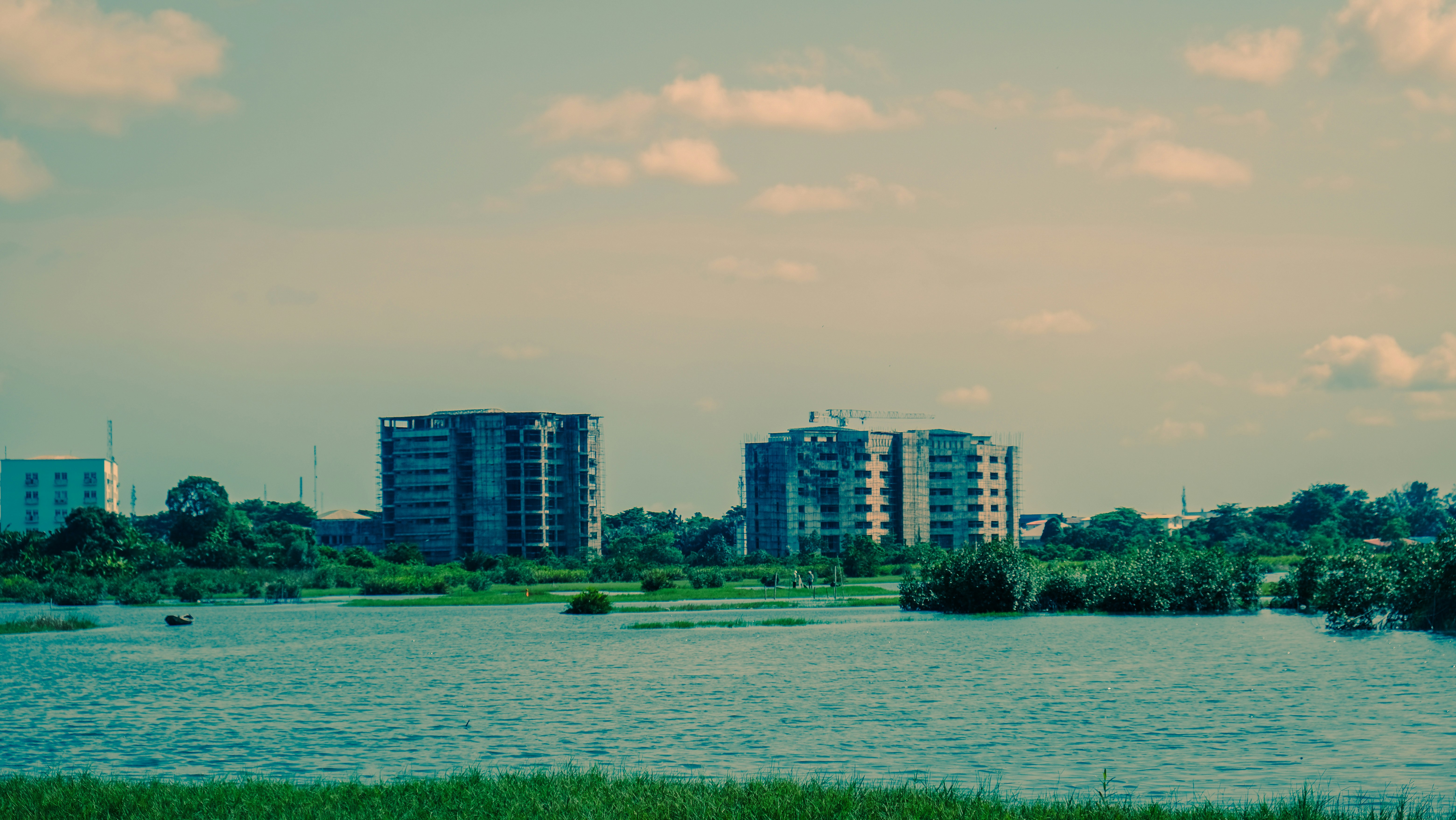 Modern buildings rise above a serene lake and green reeds.