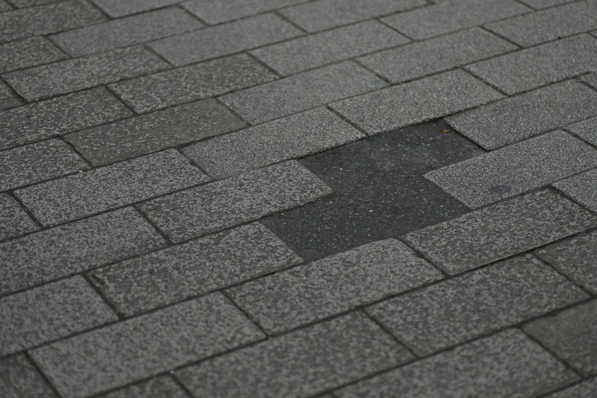 Close view of a gray asphalt shingle roof with a section of shingles missing and the dark layer underneath showing