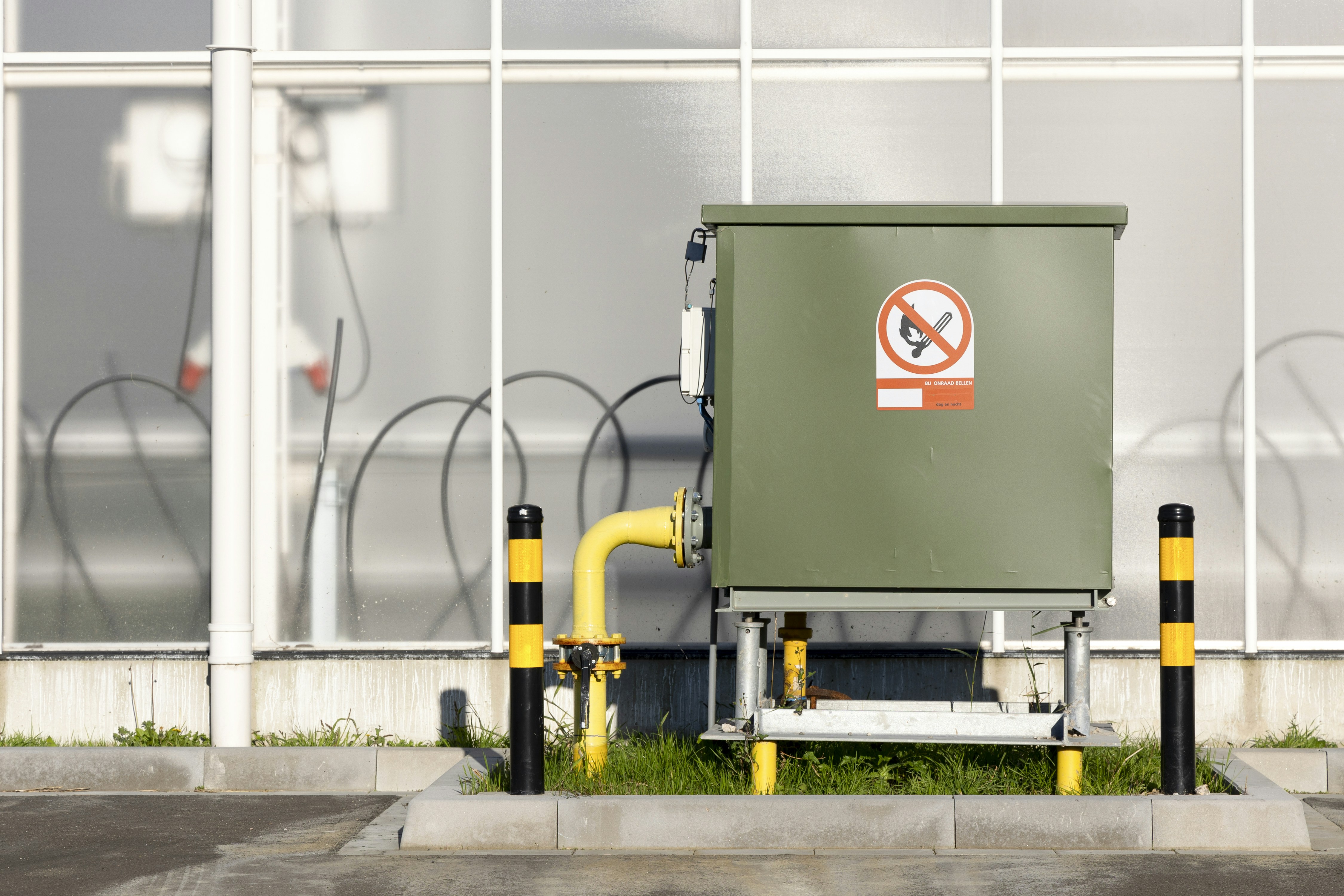 Green utility box with no smoking sign and yellow pipe.