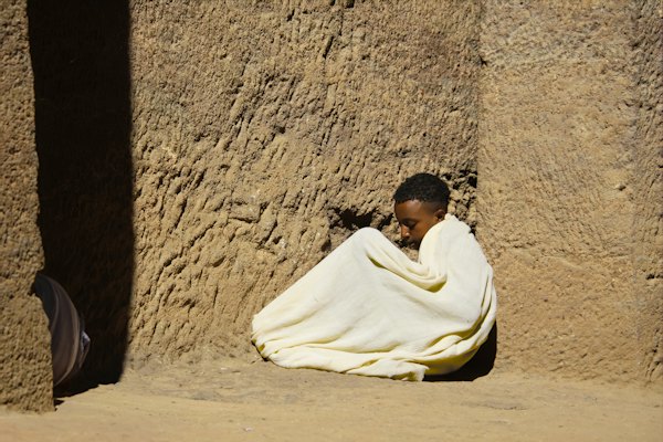 Person in white robe sits against a textured wall — Lalibela, Ethiopia