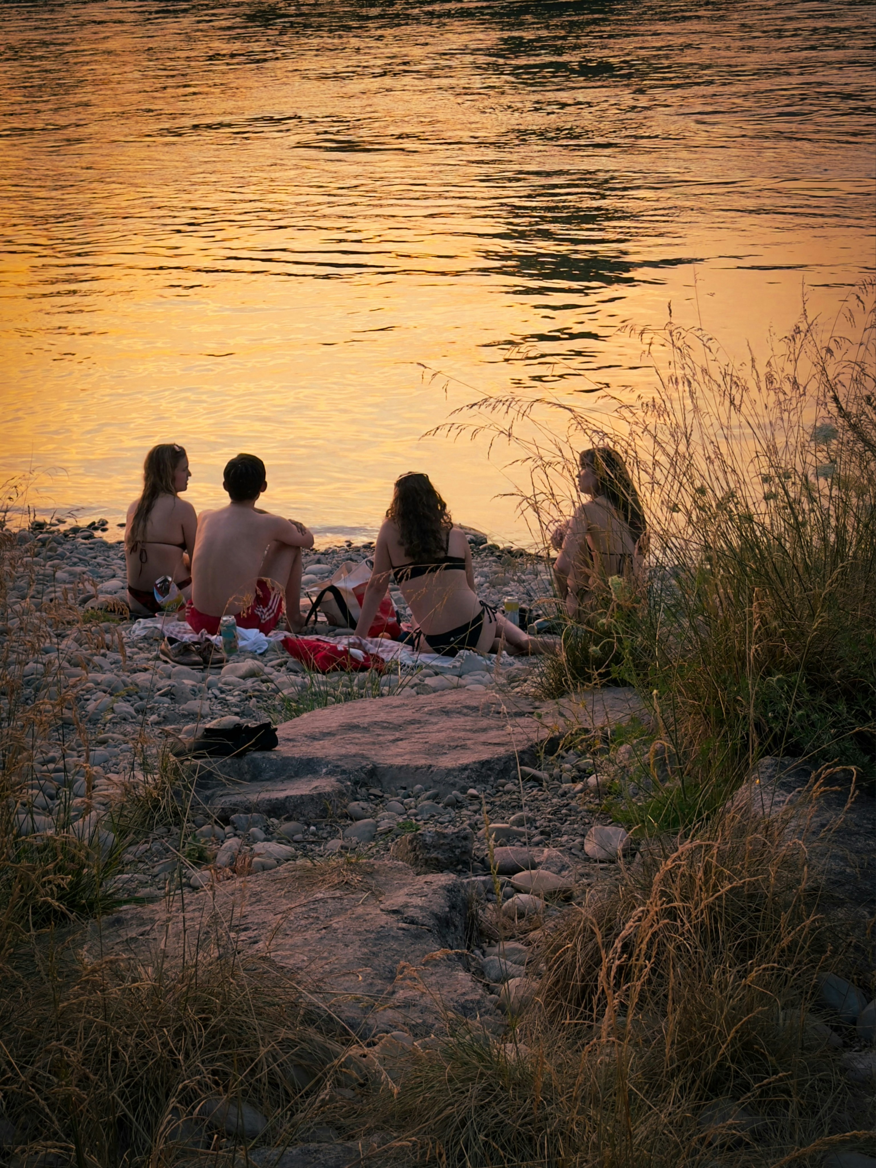 Four people relax by the water at sunset