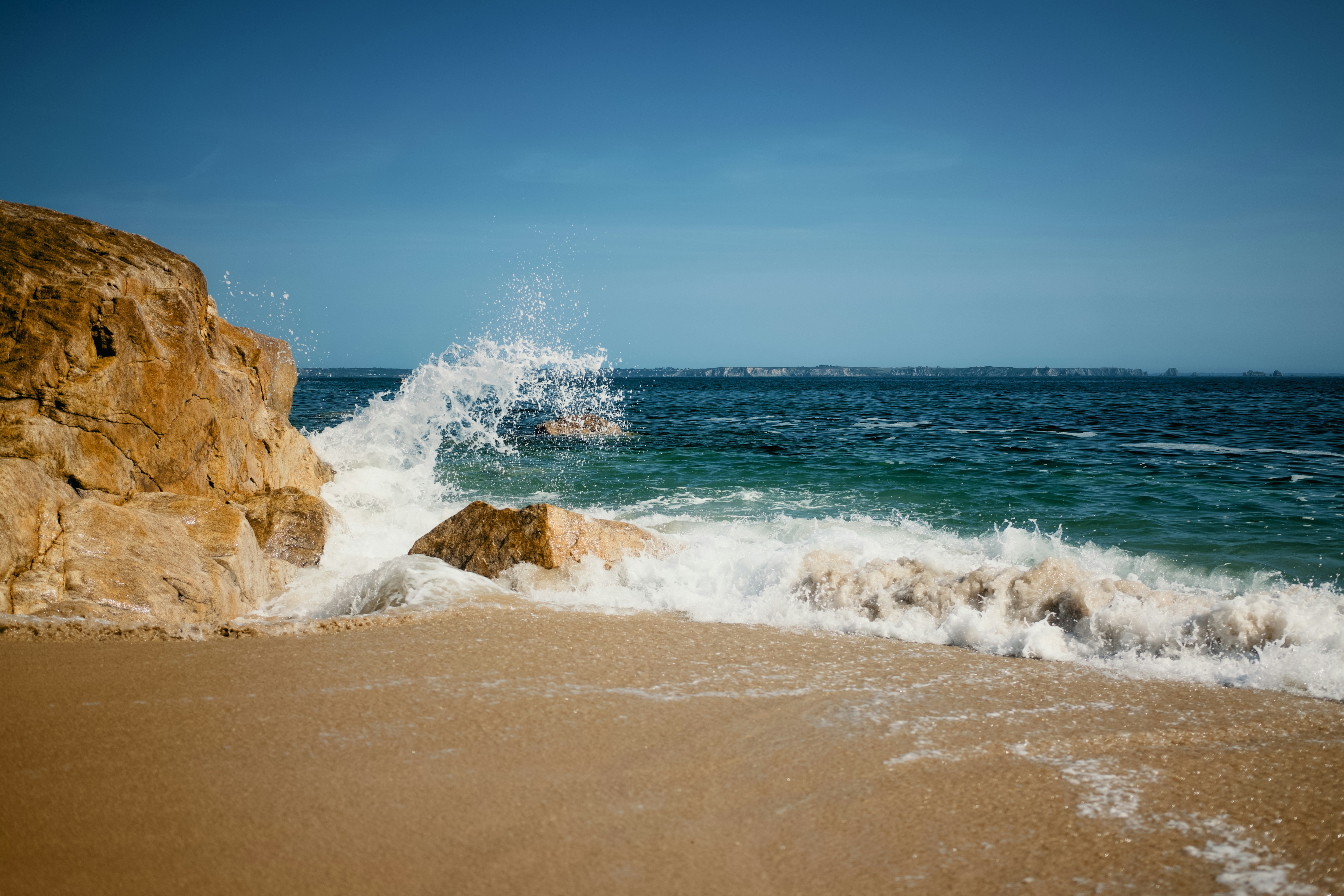 Ocean waves crash against a sandy beach and rocky cliff.