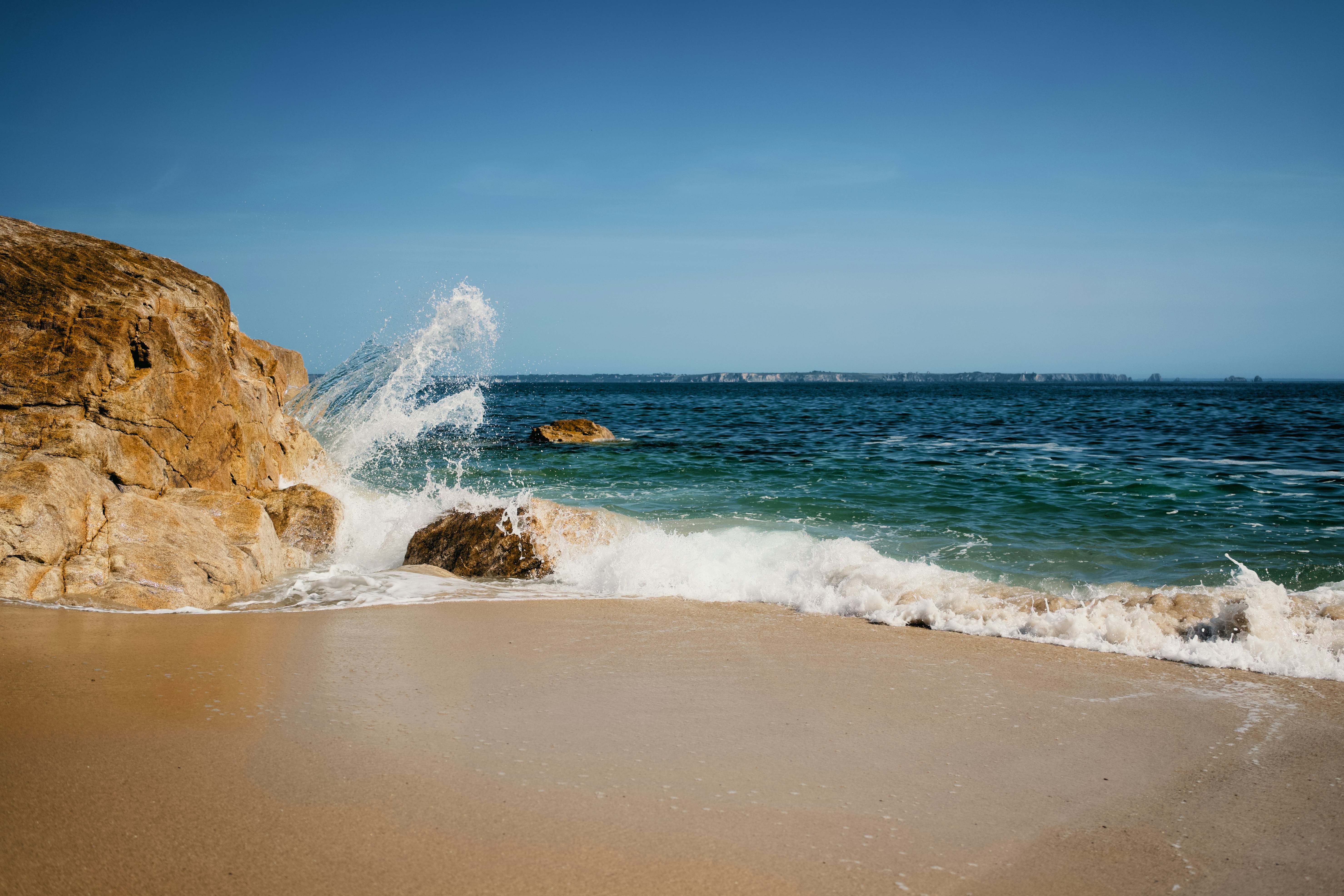 Waves crash against a rocky shore on a sunny day.