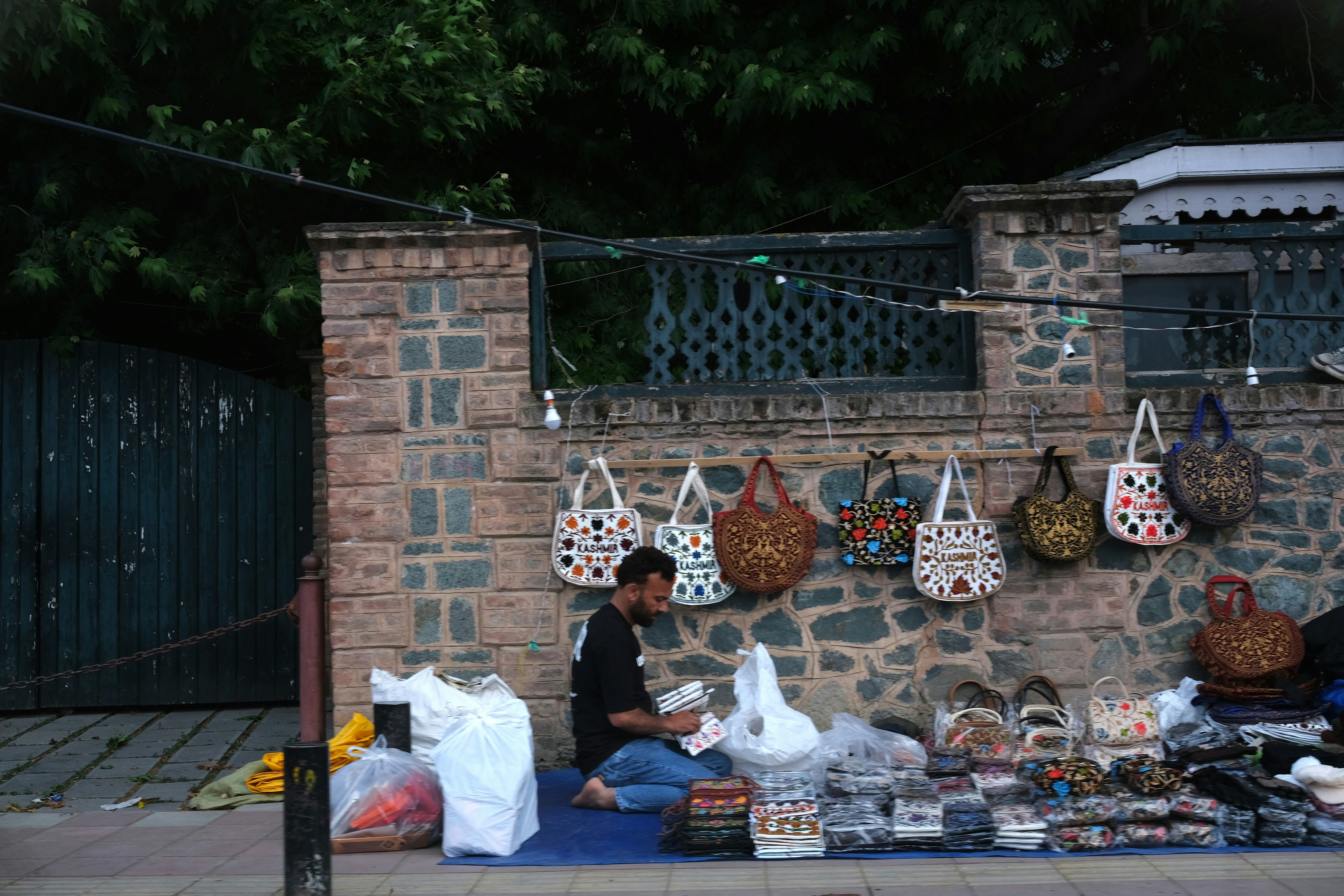 Vendedor vendendo bolsas e itens expostos em uma parede de pedra.