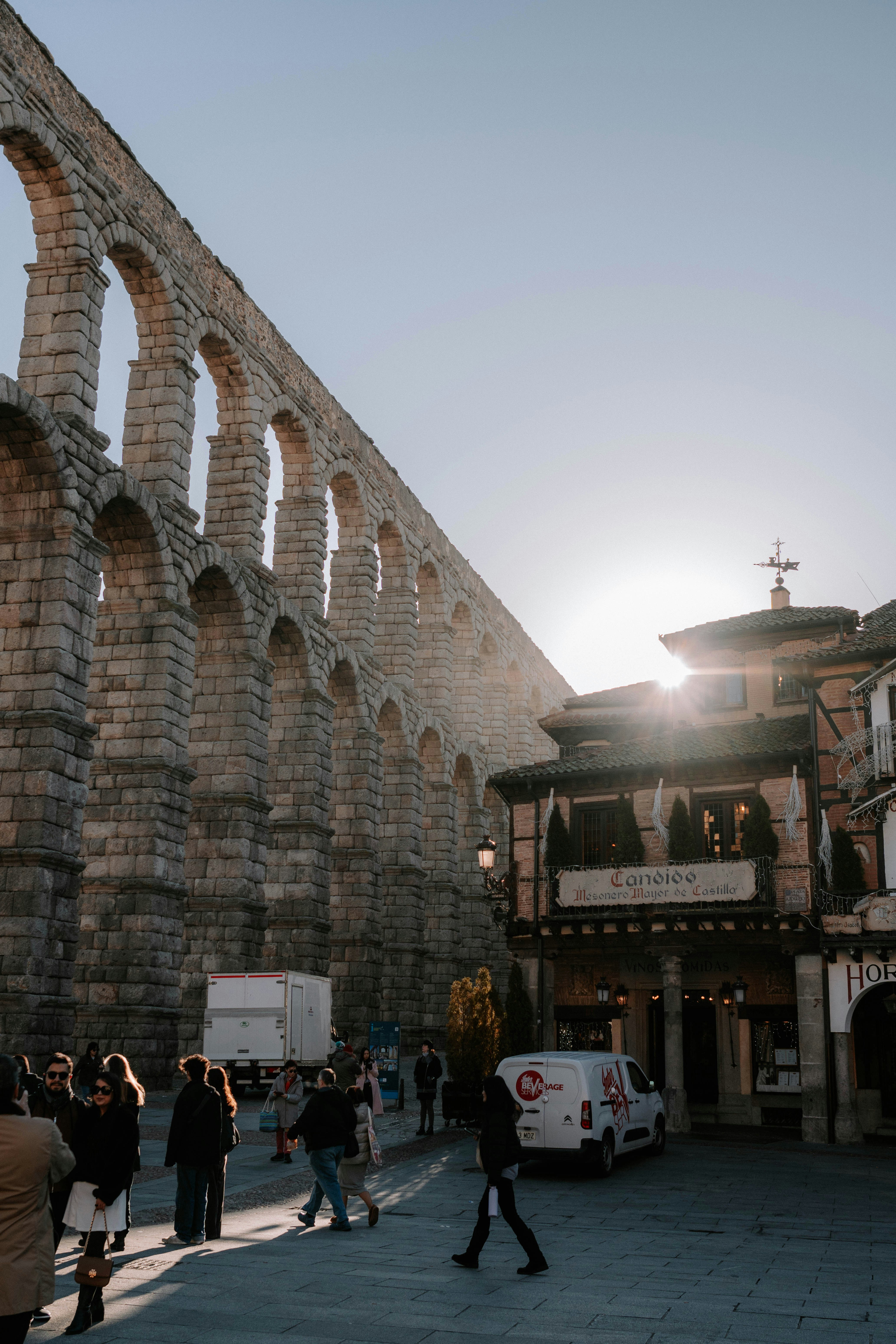 Historic roman aqueduct and buildings with people at sunset.