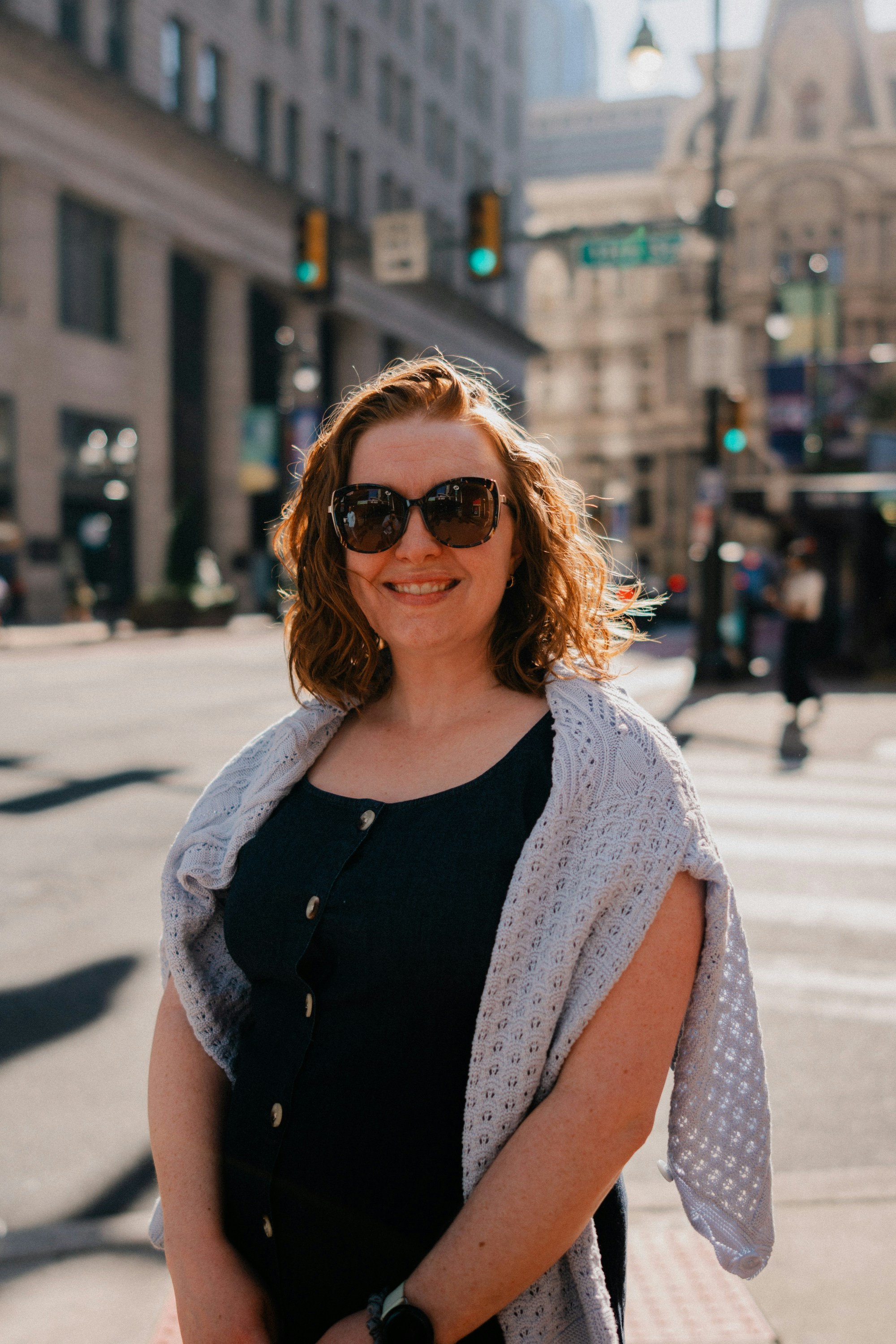 Smiling woman in sunglasses on a sunny city street.