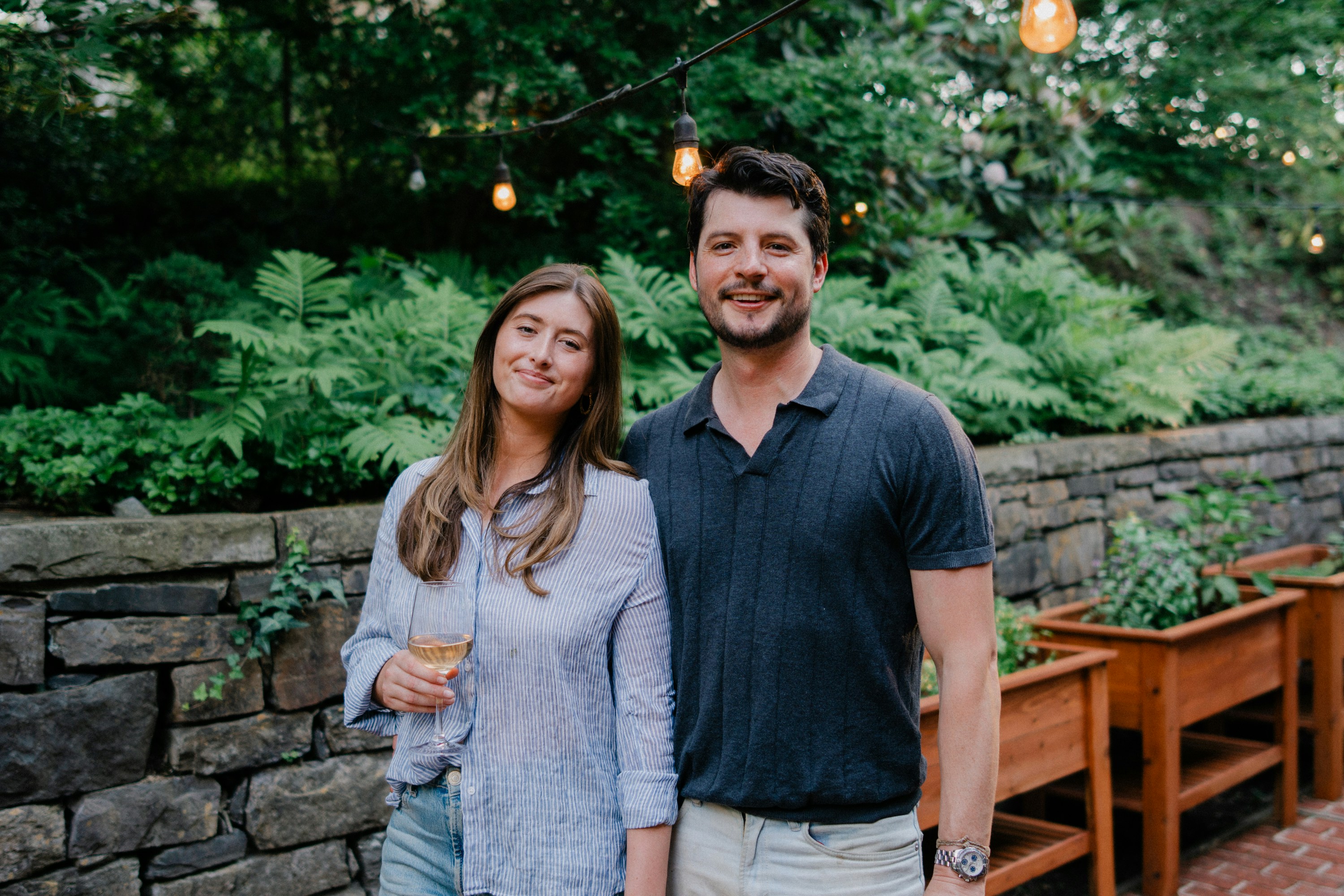 A smiling couple stands in a lush outdoor patio.