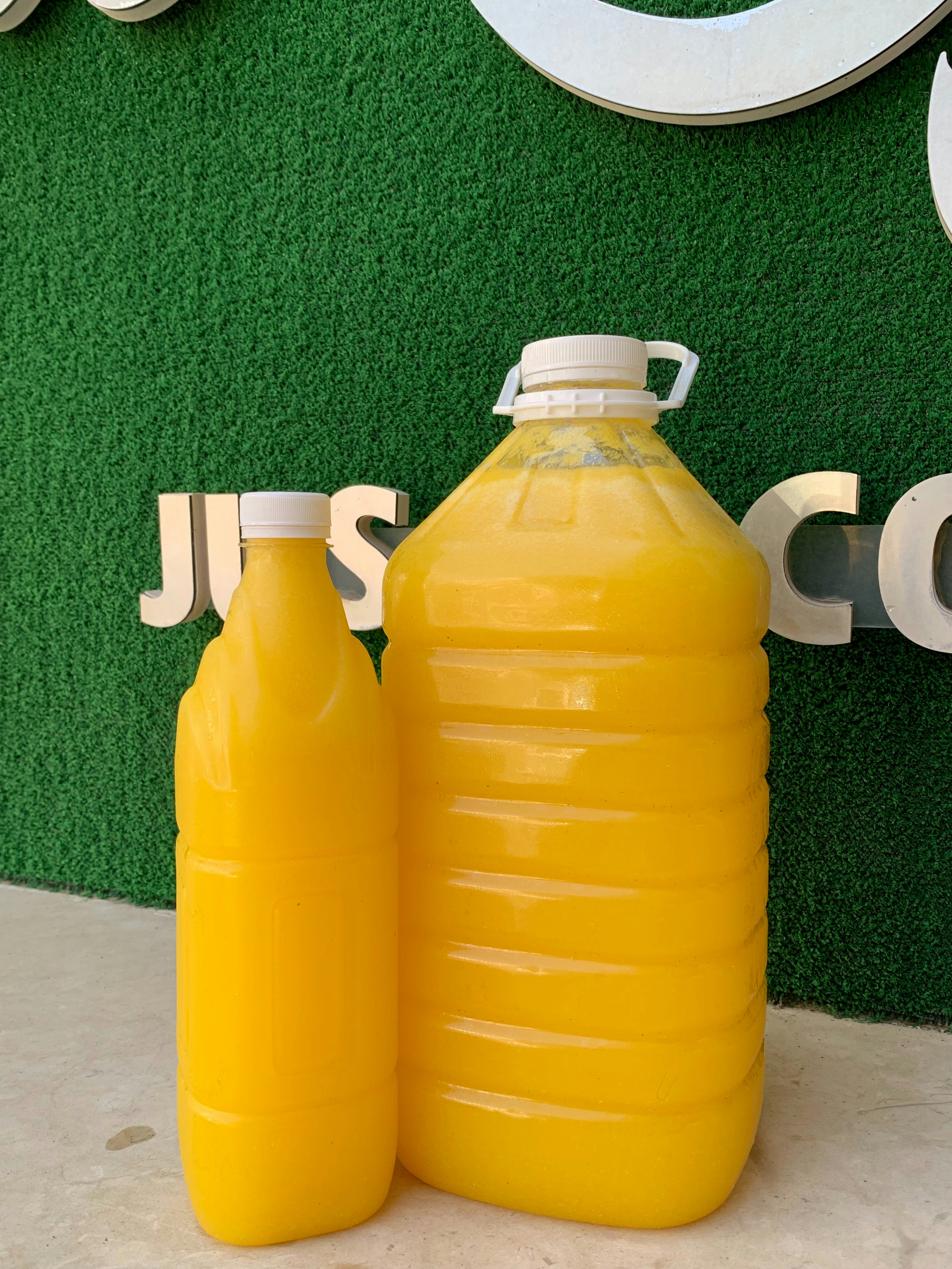 Two plastic bottles filled with orange liquid against green.