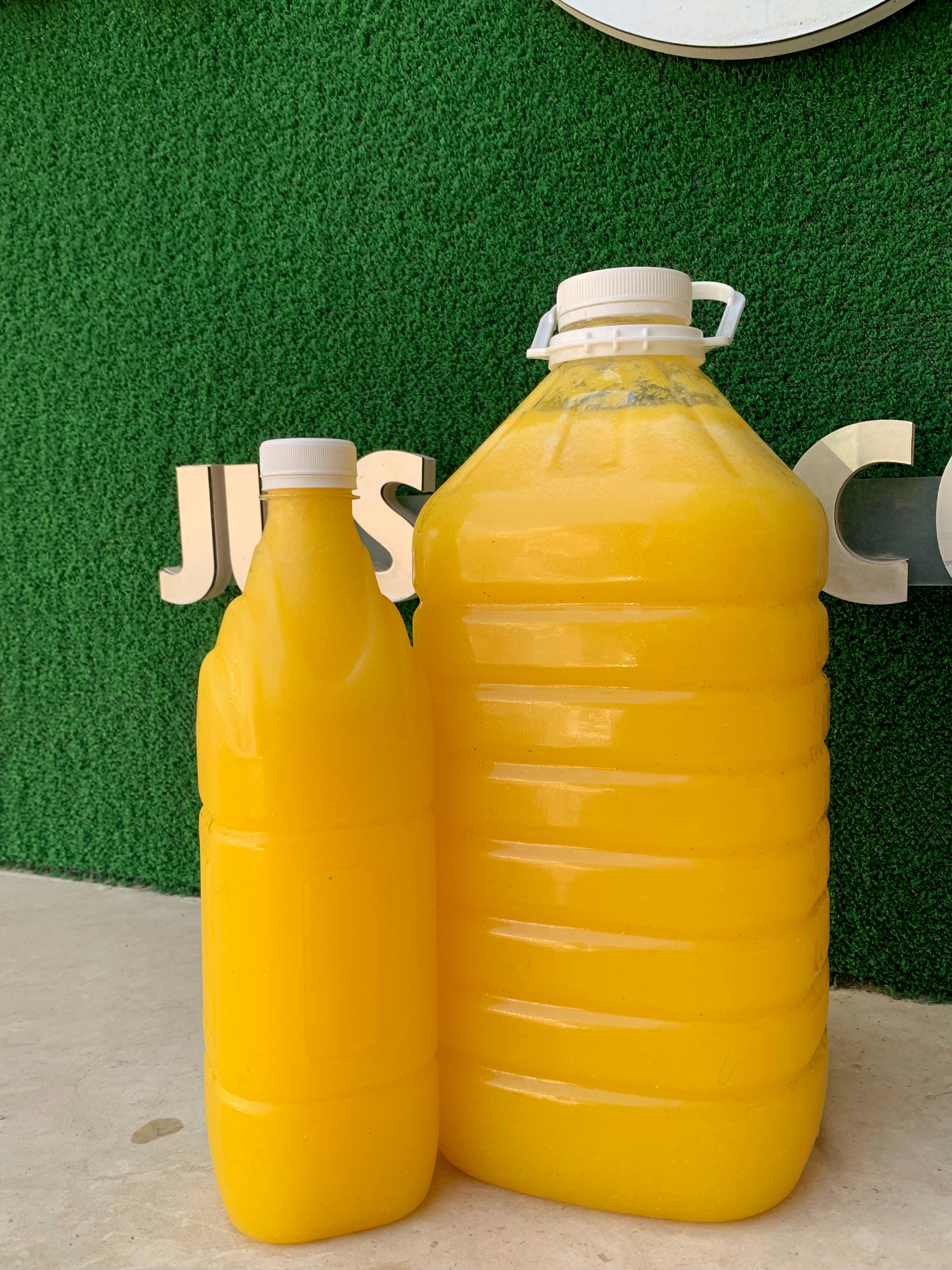 Two plastic bottles of orange juice against a green background.