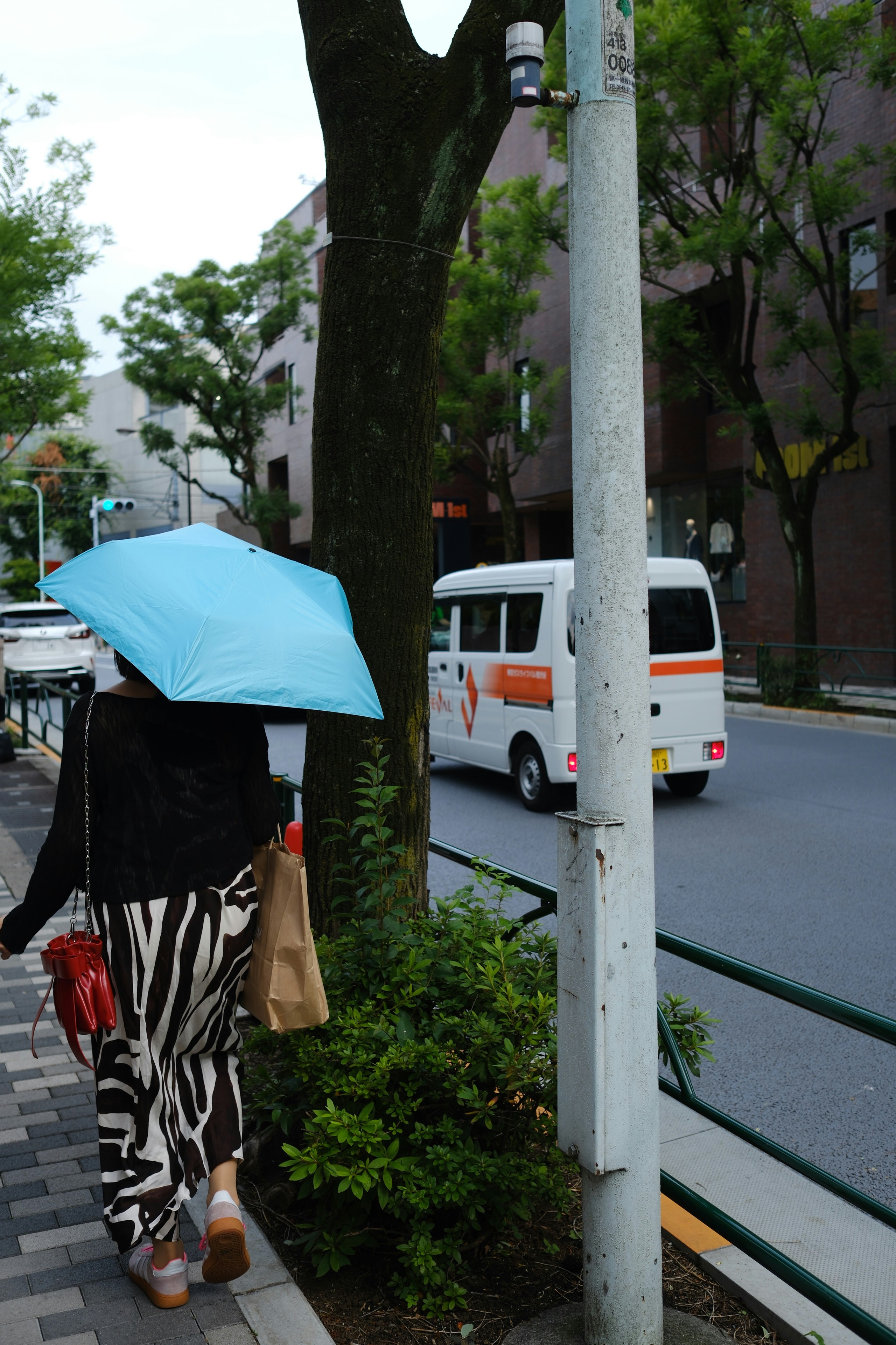 Une personne avec un parapluie bleu marche dans une rue de la ville.