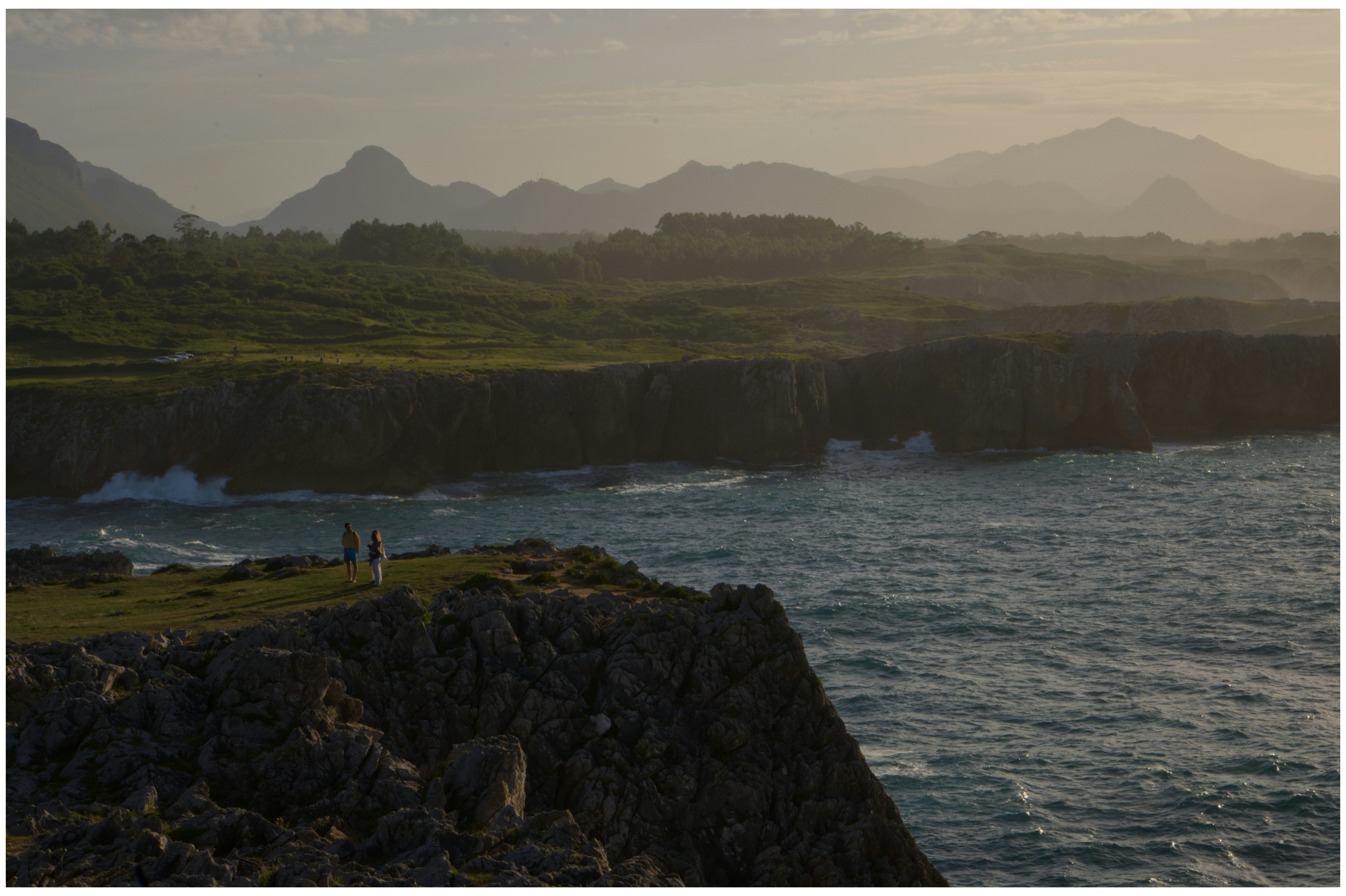 Acantilados de la costa cántabra al atardecer, con prados verdes y el mar rompiendo contra las rocas