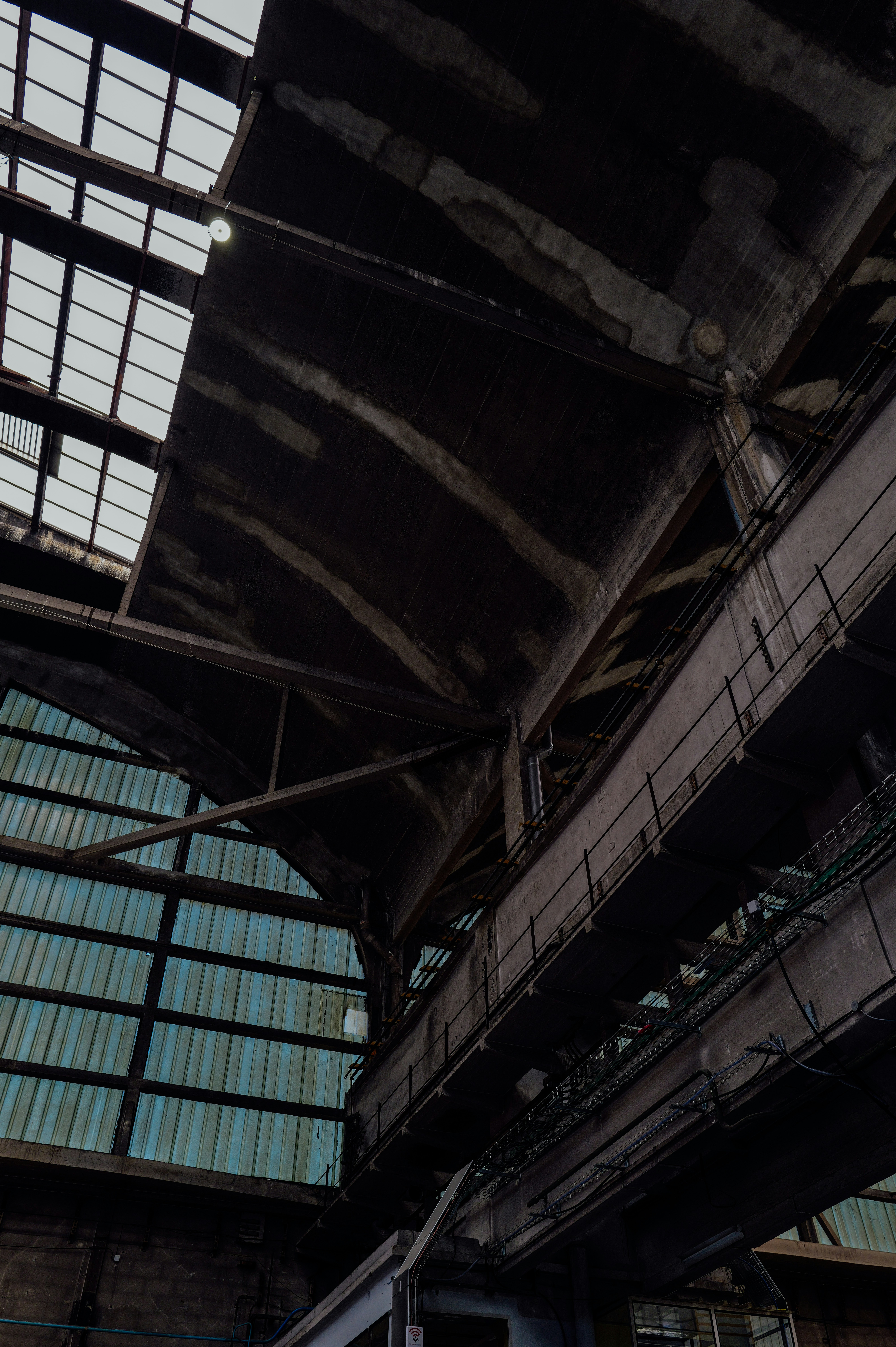 Interno di edificio industriale fatiscente con struttura metallica e finestre a vista.