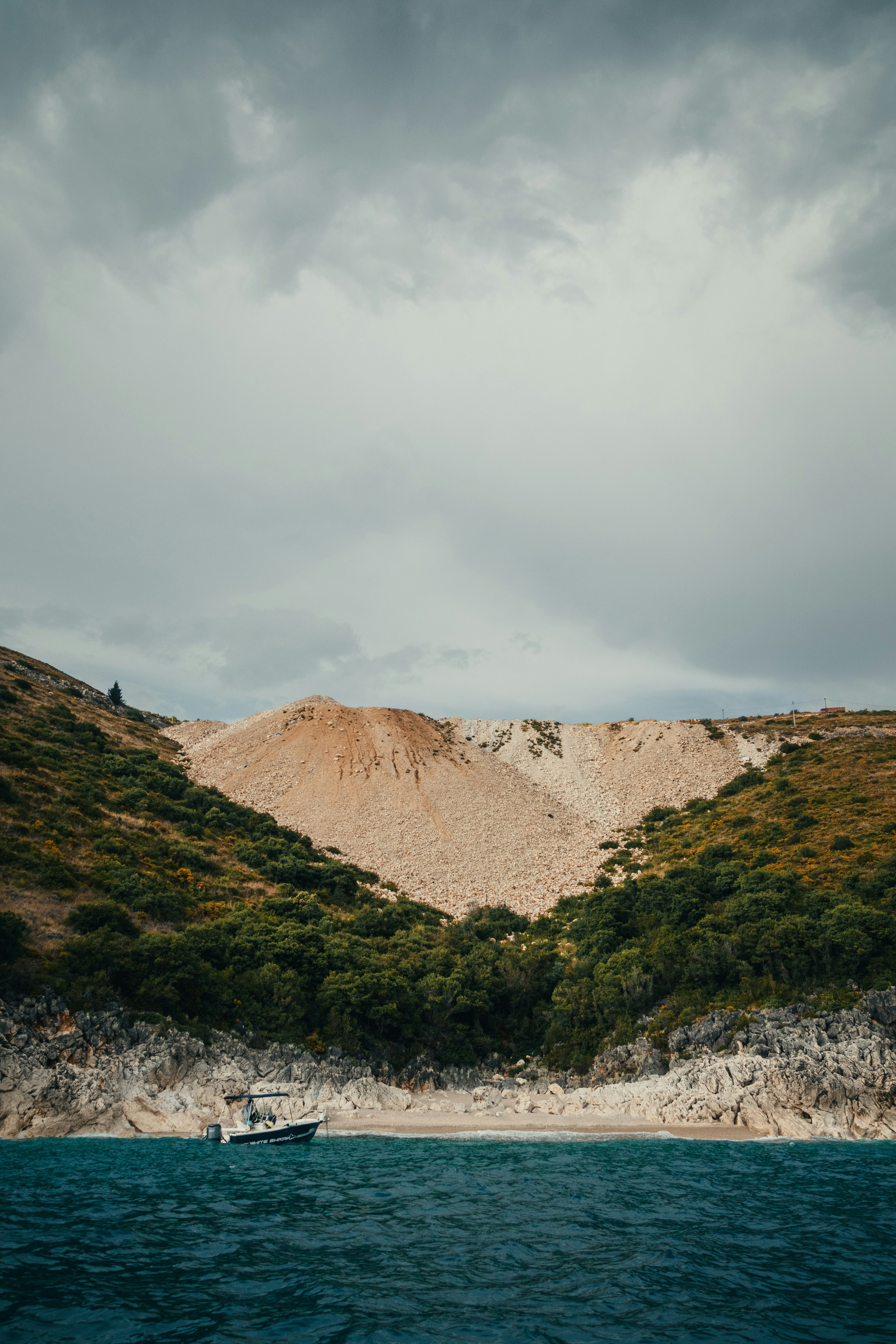 Small boat on rocky shore beneath hills and cloudy sky
