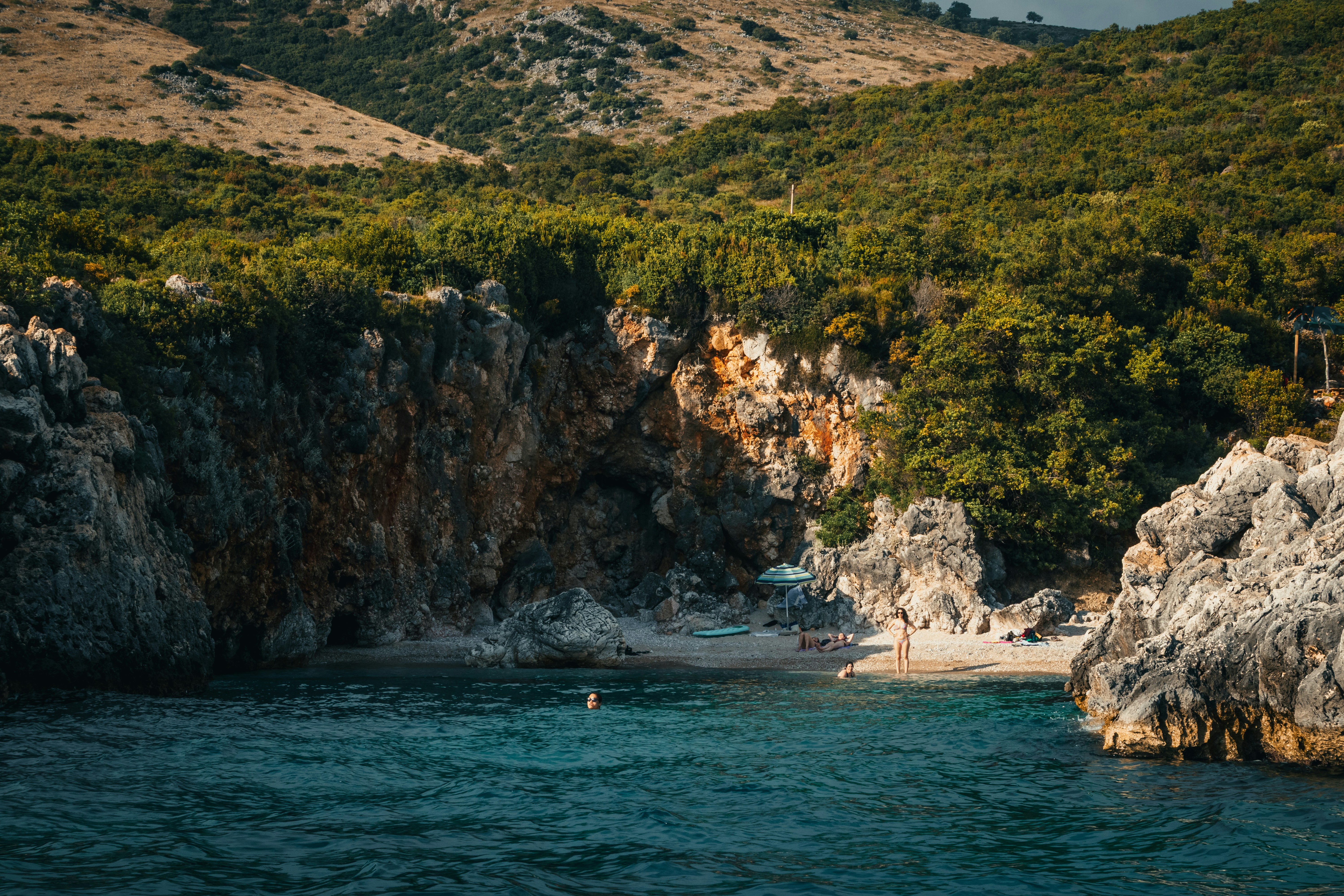 Secluded bay with clear blue water, rocky cliffs, green hills