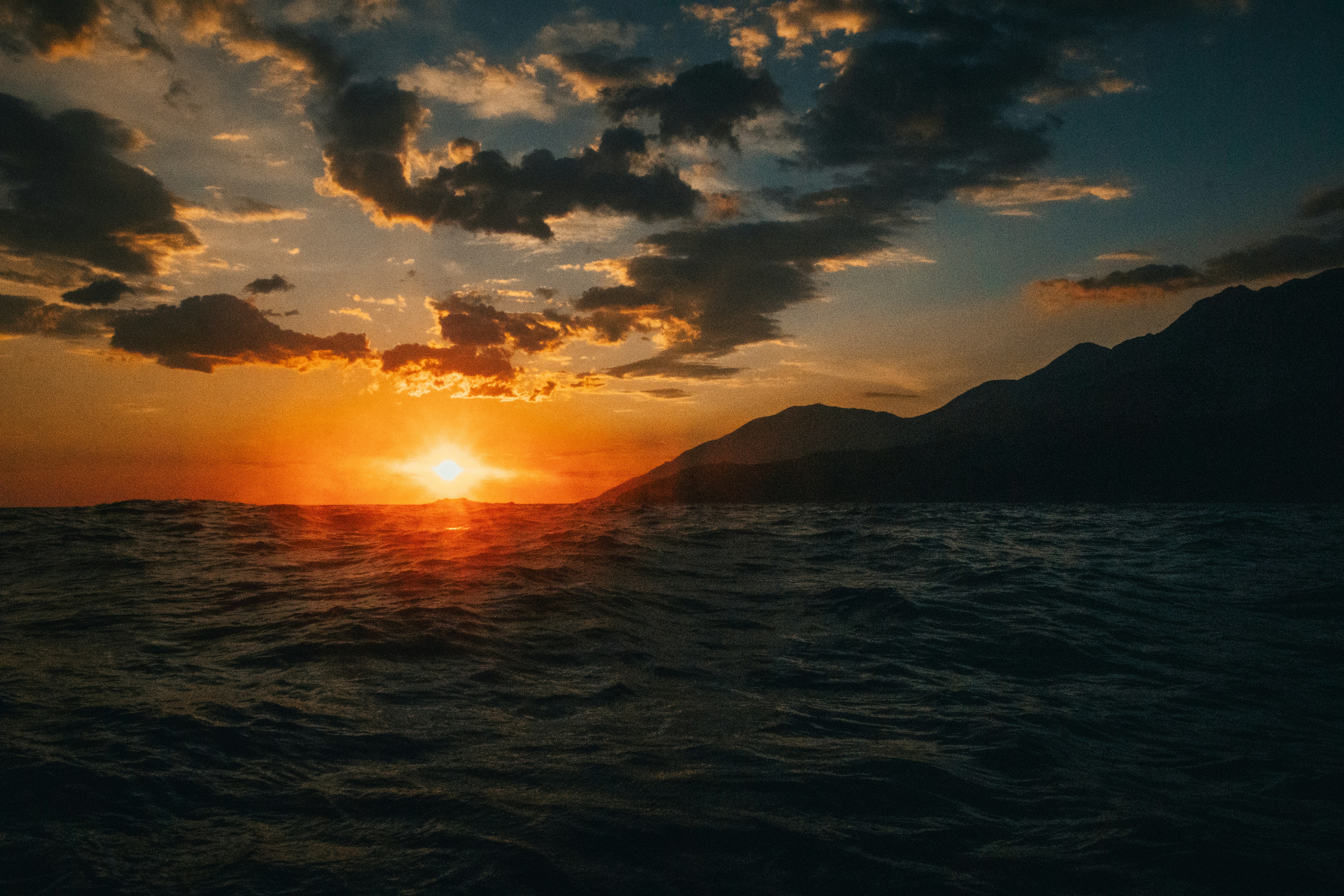 Golden sunset over a dark, wavy ocean with mountains