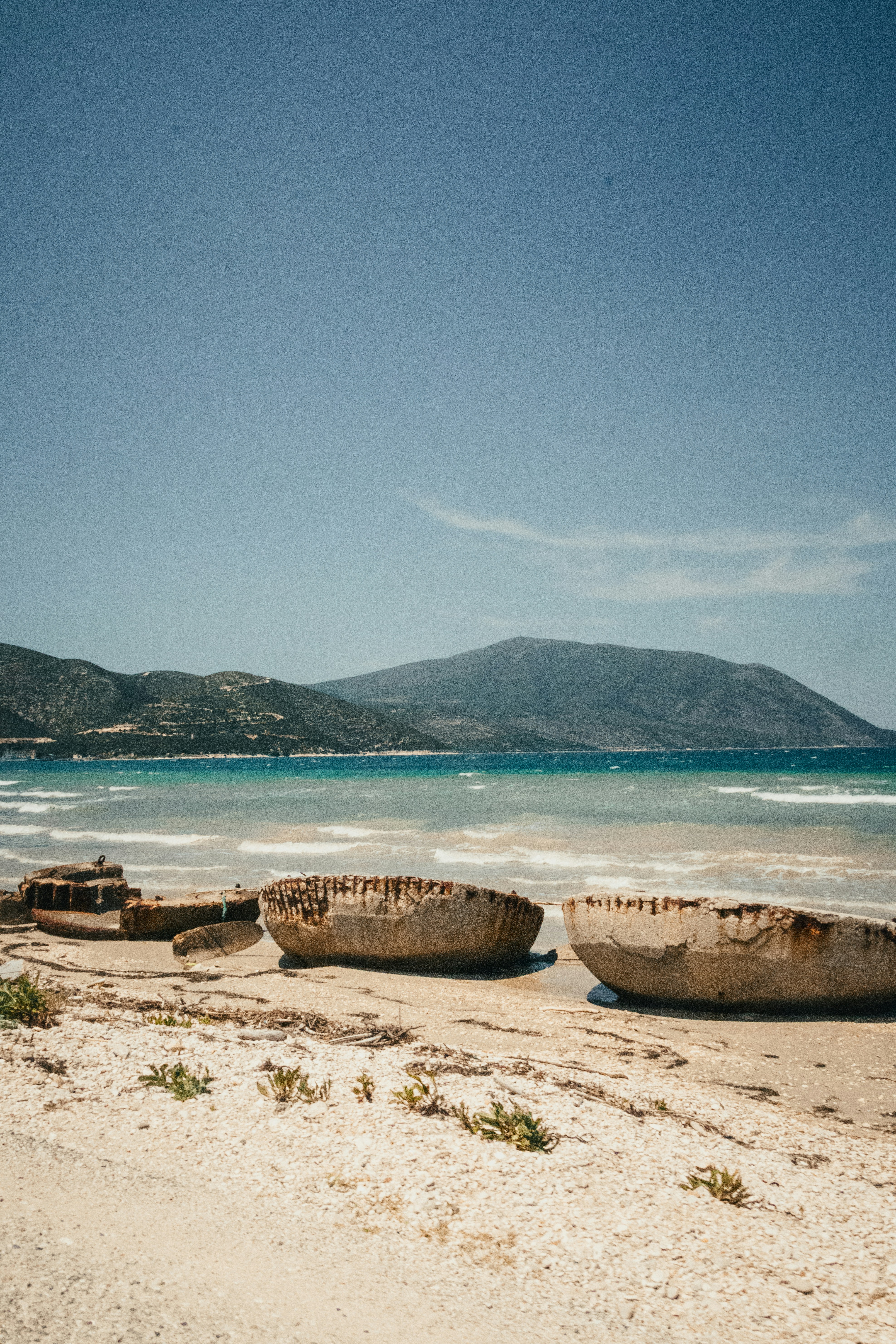 Weathered boat hulls on a beach with ocean and mountains