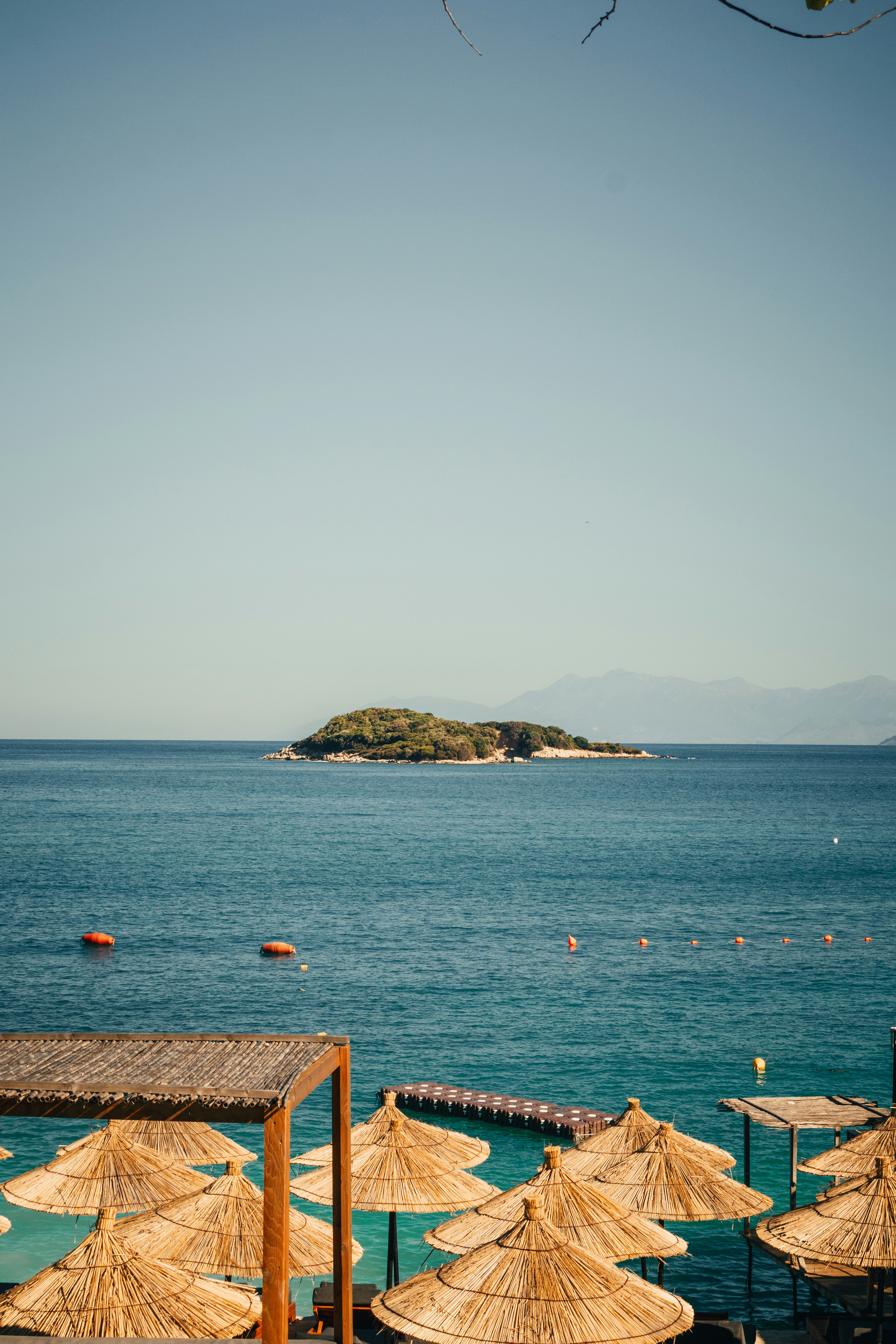 Straw umbrellas by a blue ocean with a small island