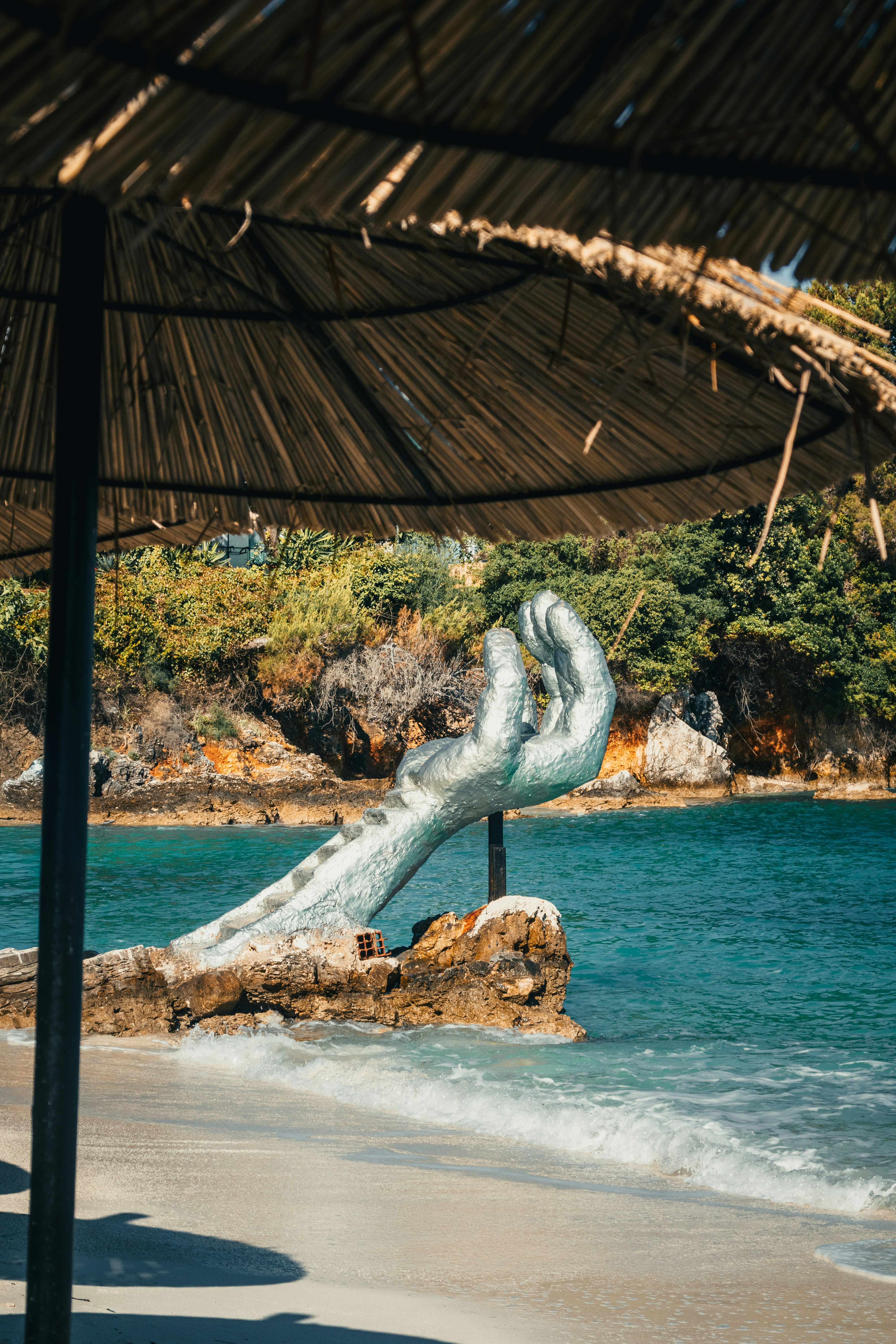 Hand sculpture emerges from the sea on a sunny beach