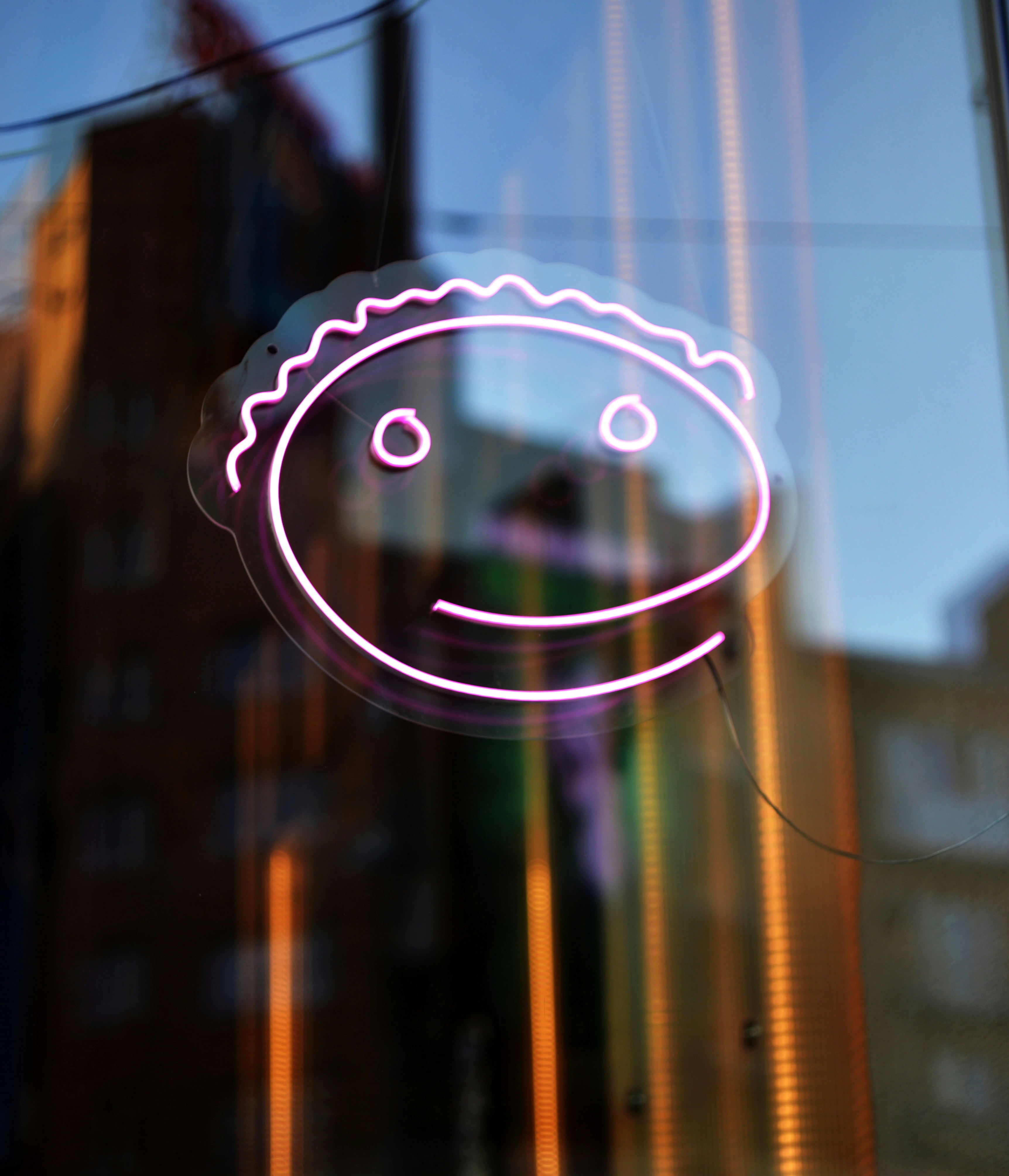 A pink neon smiling face sign on a reflective window.