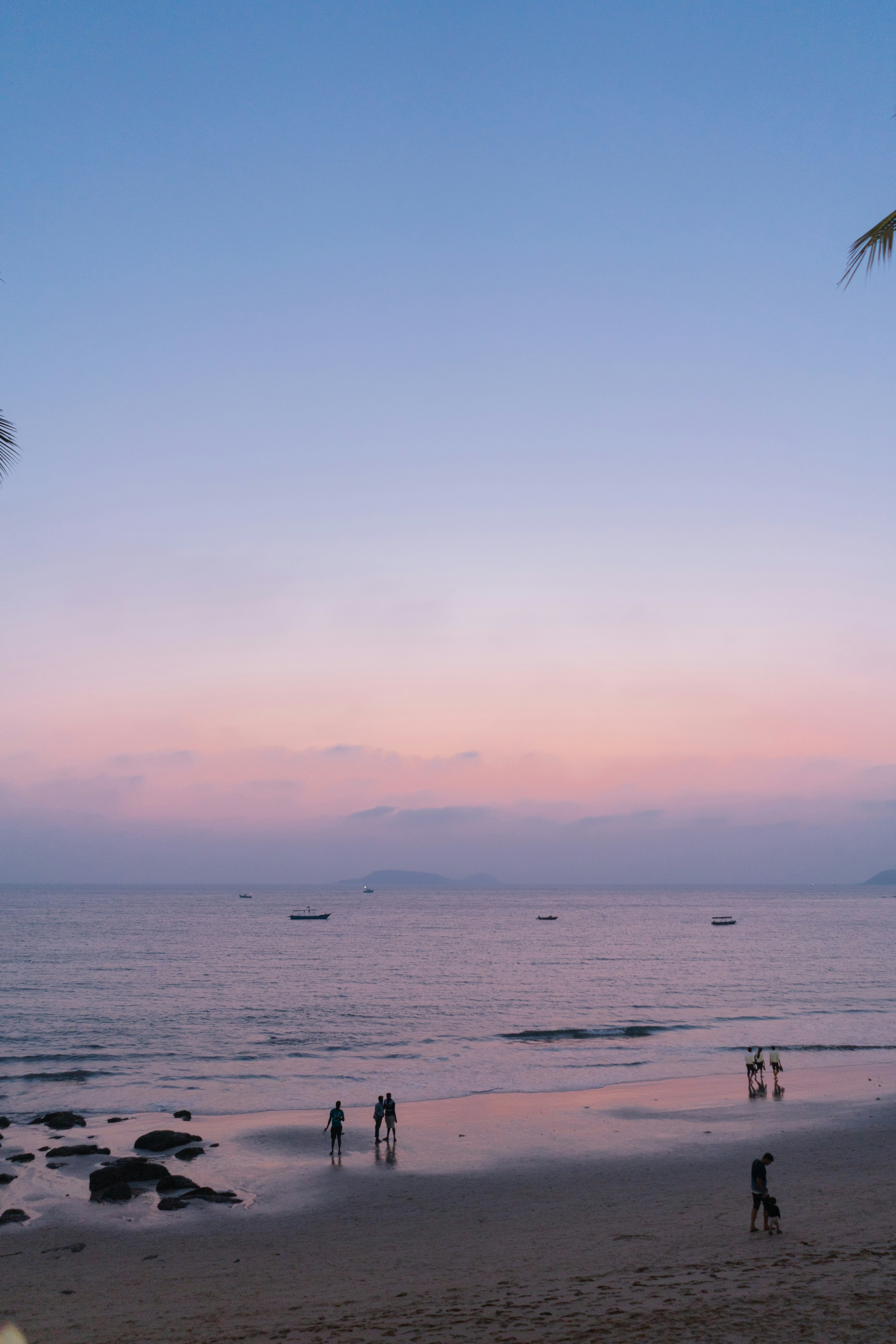 Pessoas em uma praia ao pôr do sol com um oceano calmo.