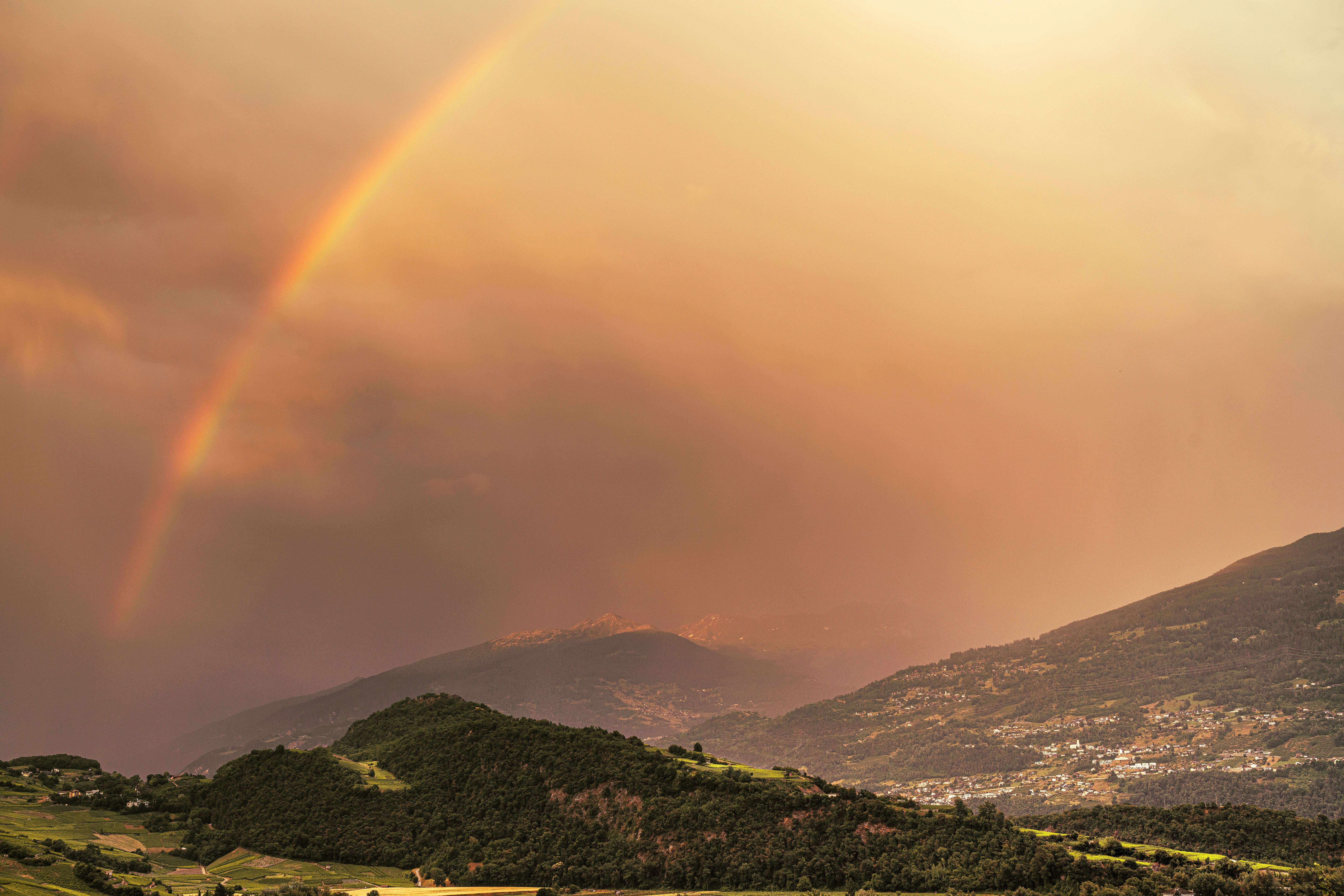 Un vibrante arcobaleno si erge sopra montagne verdi e una valle.