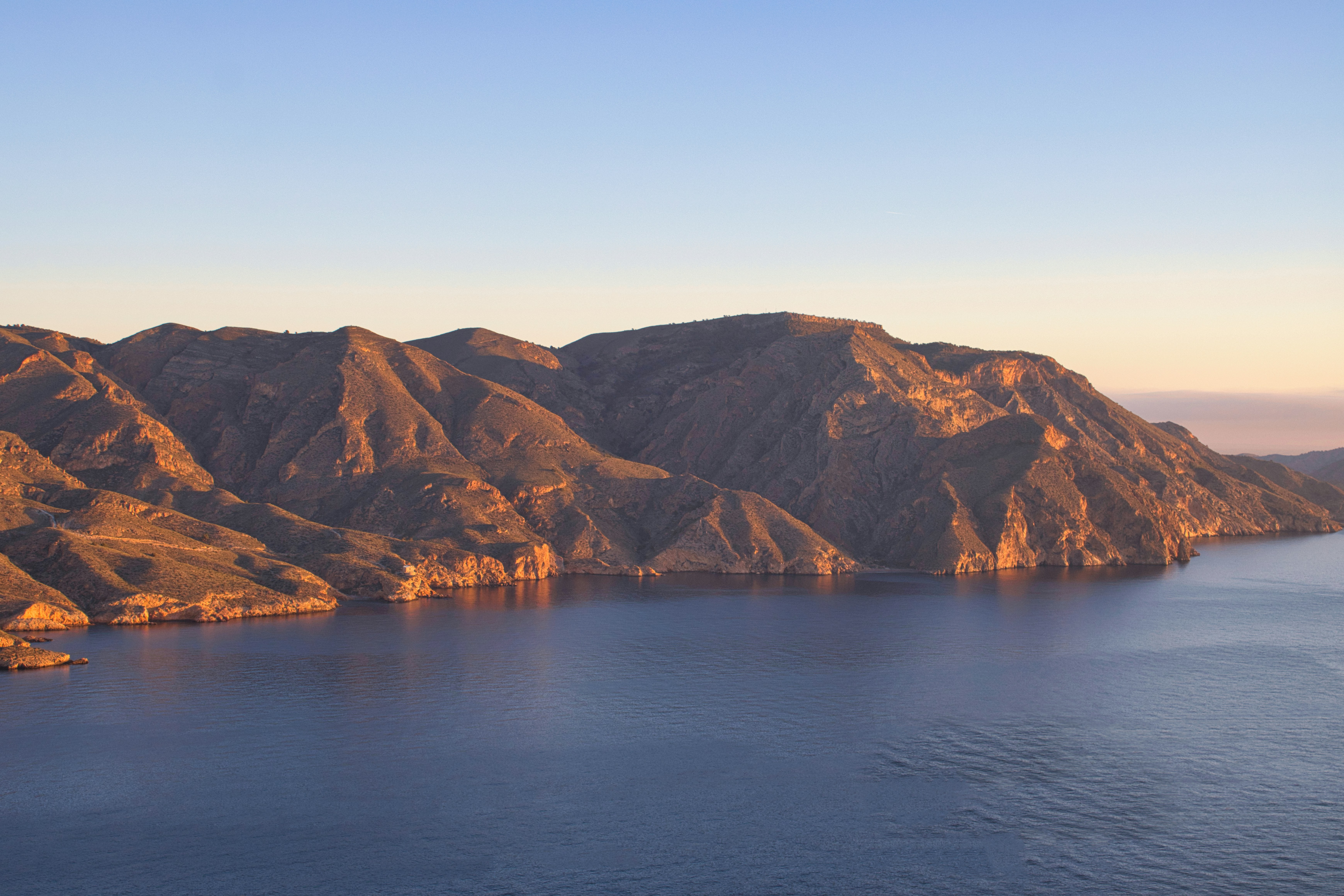 Rugged mountains meet the calm ocean under a clear sky.