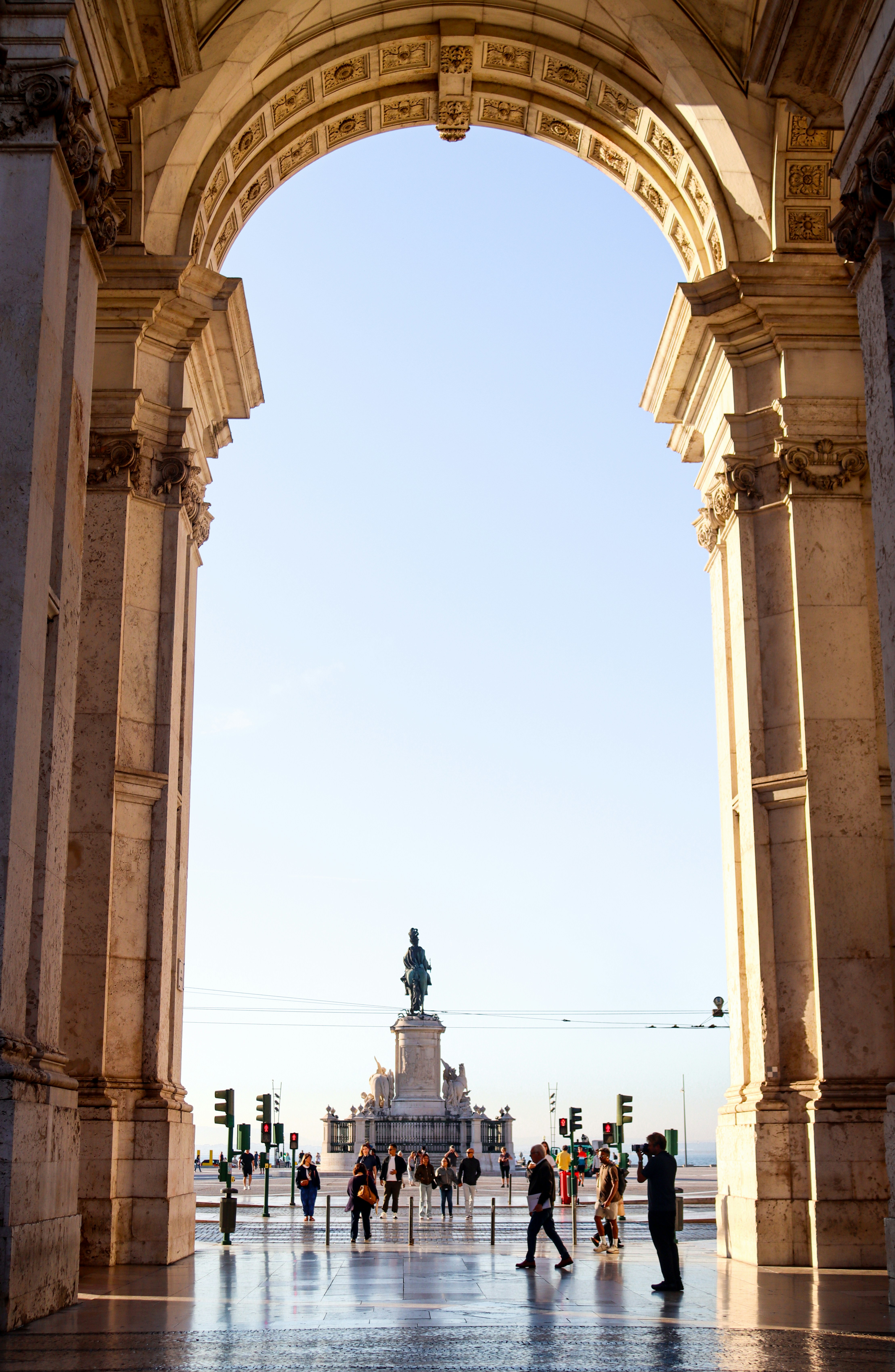 People walk through an archway towards a distant statue.
