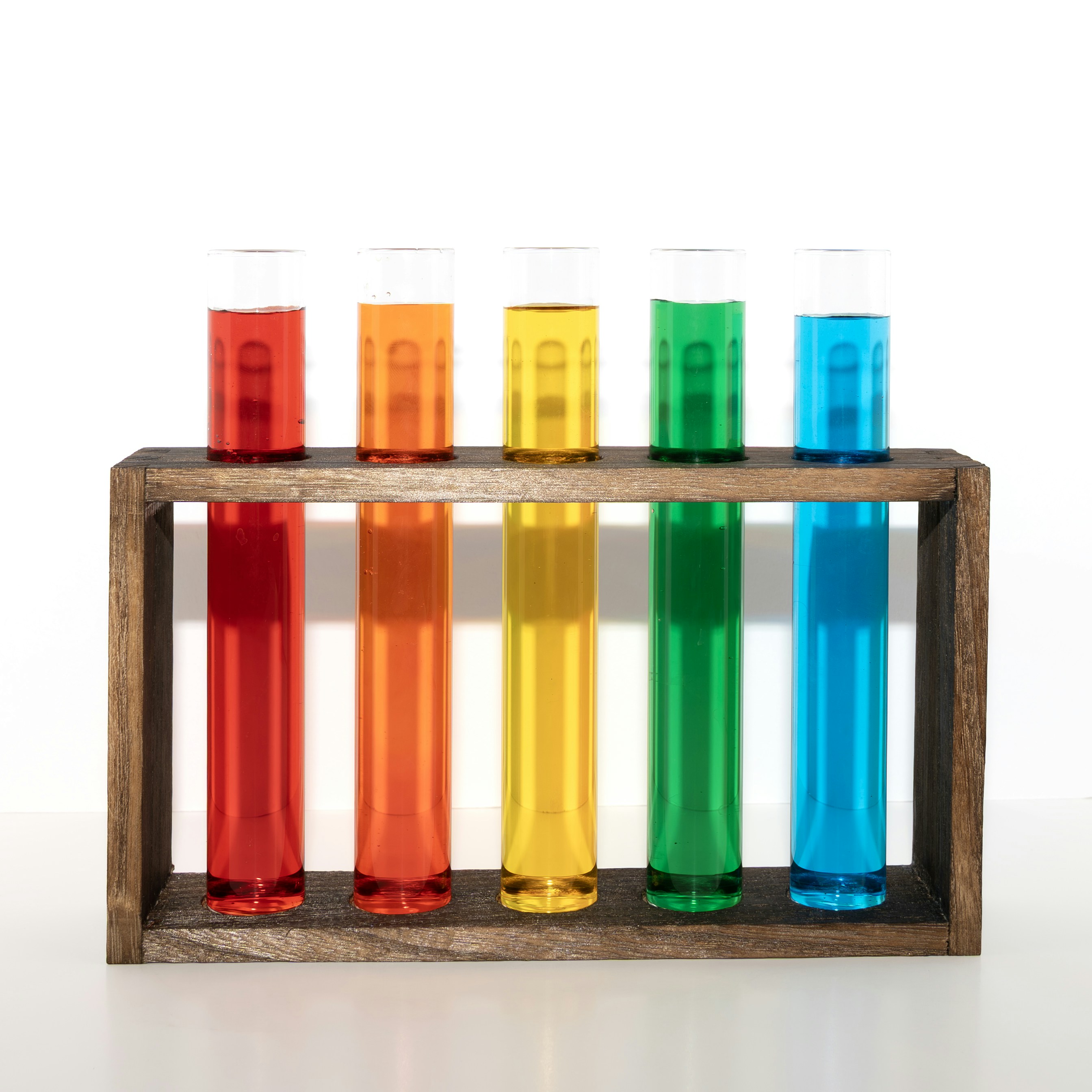 Five test tubes with colorful liquids in a wooden rack.