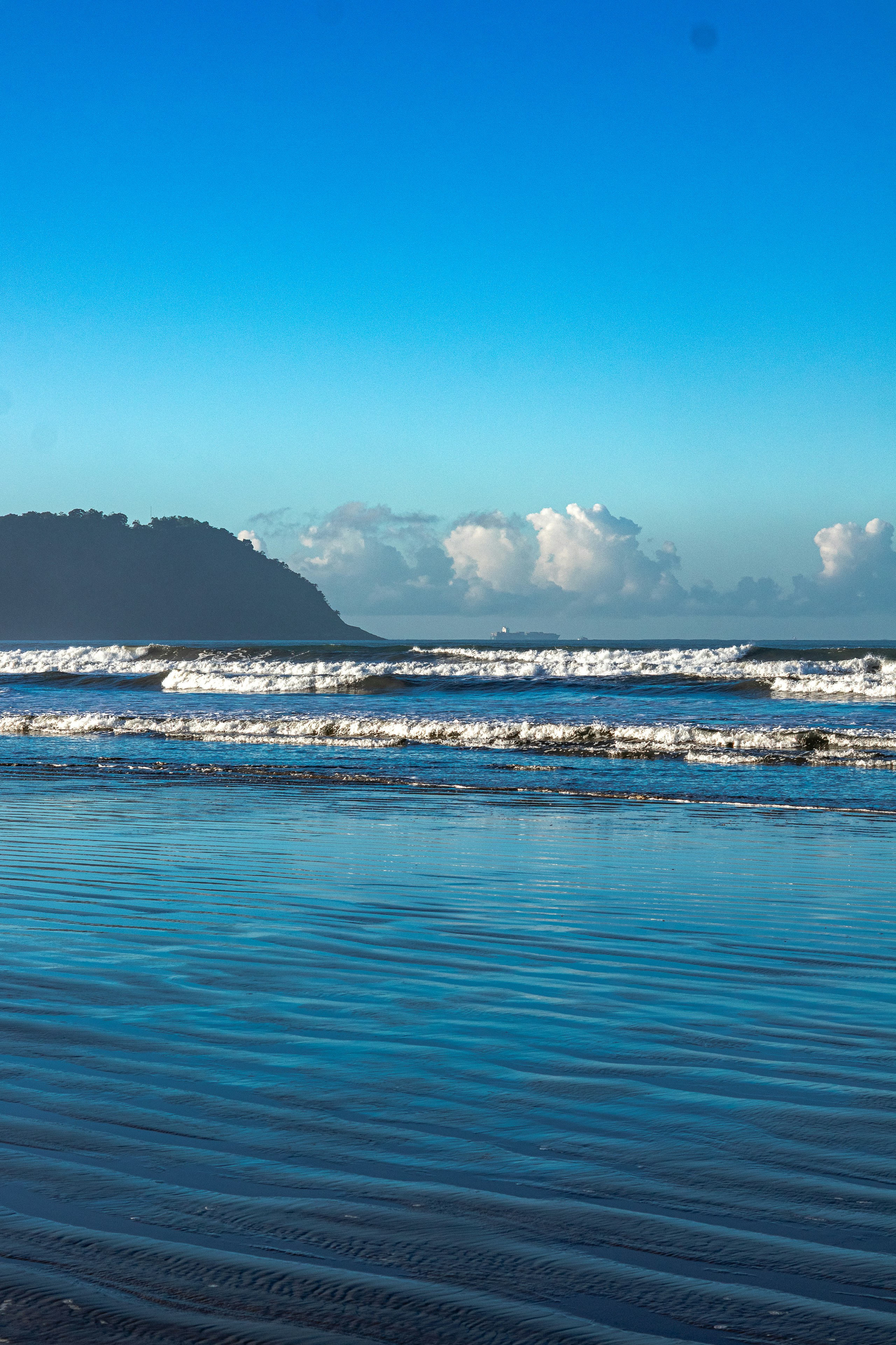 Ombak laut biru cerah bertemu dengan pantai berpasir.