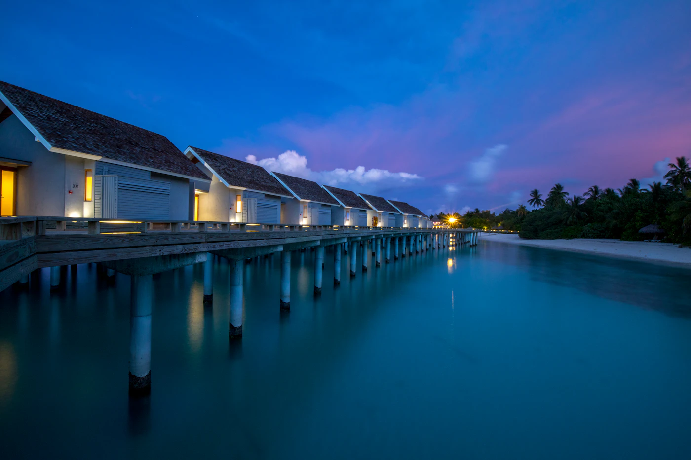 Luxury overwater villas glowing at dusk over a calm ocean