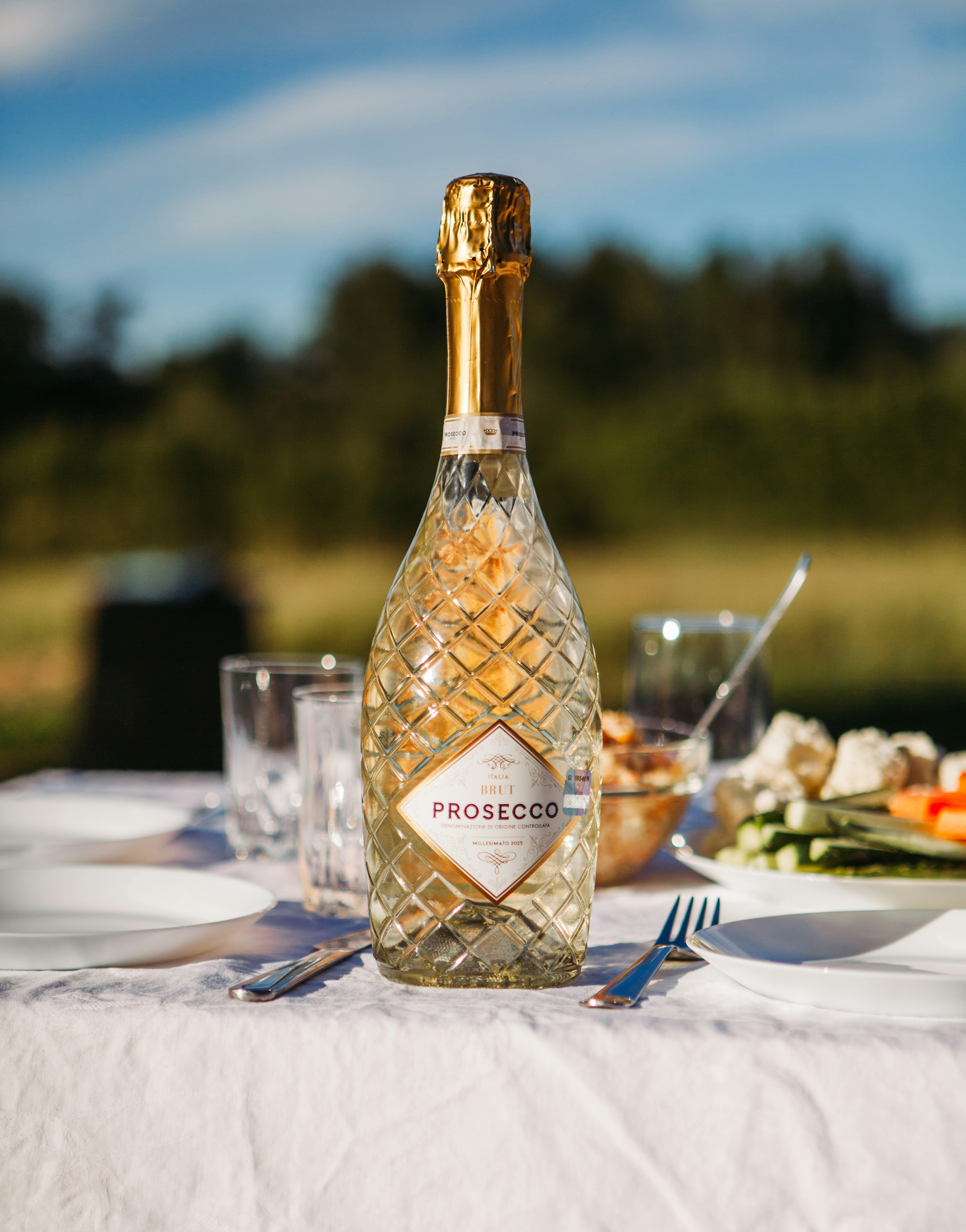 A bottle of prosecco on a white table outdoors.