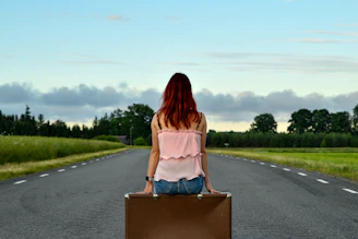 Red-haired woman sits on suitcase on empty road