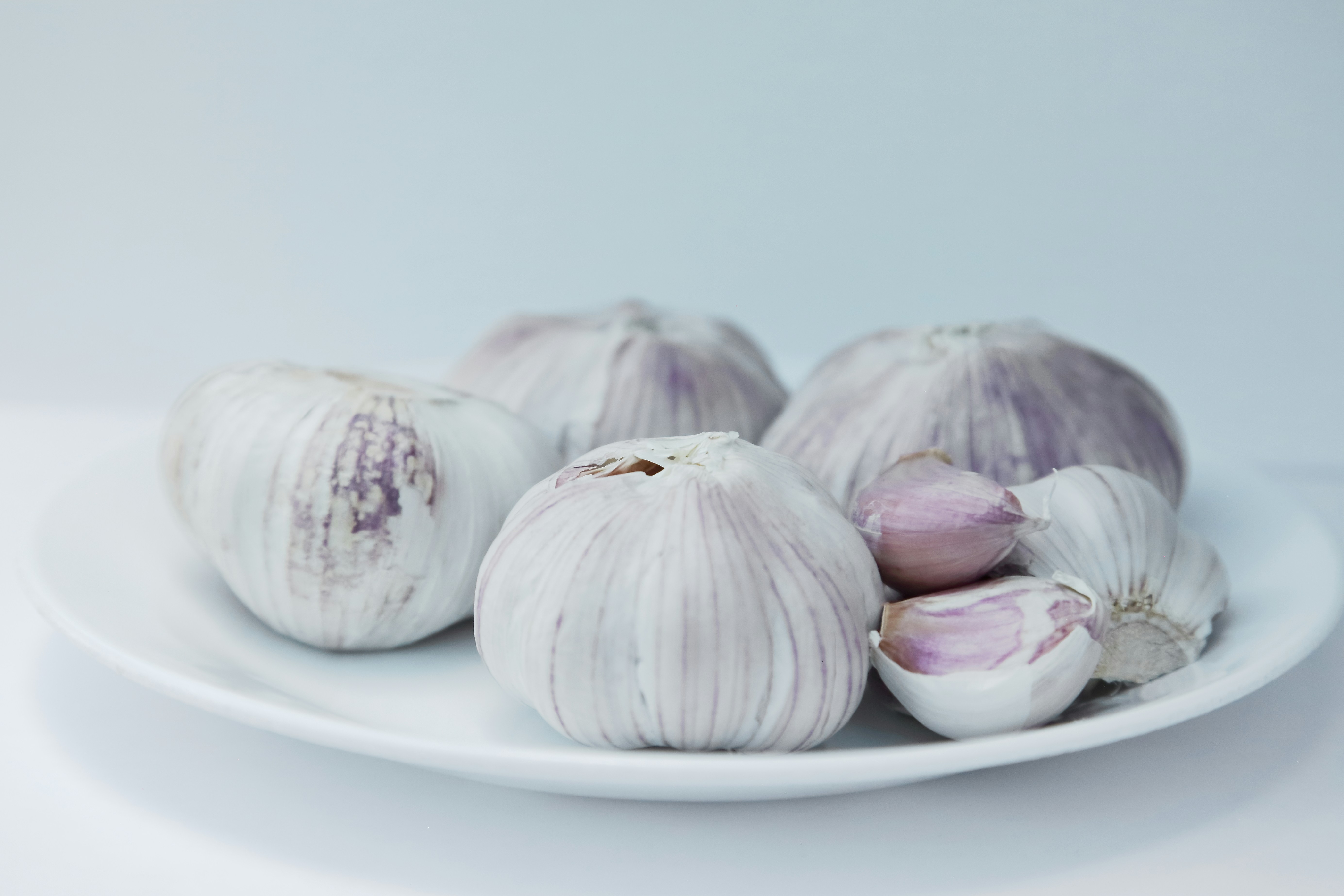Fresh garlic bulbs and cloves resting on a white plate.