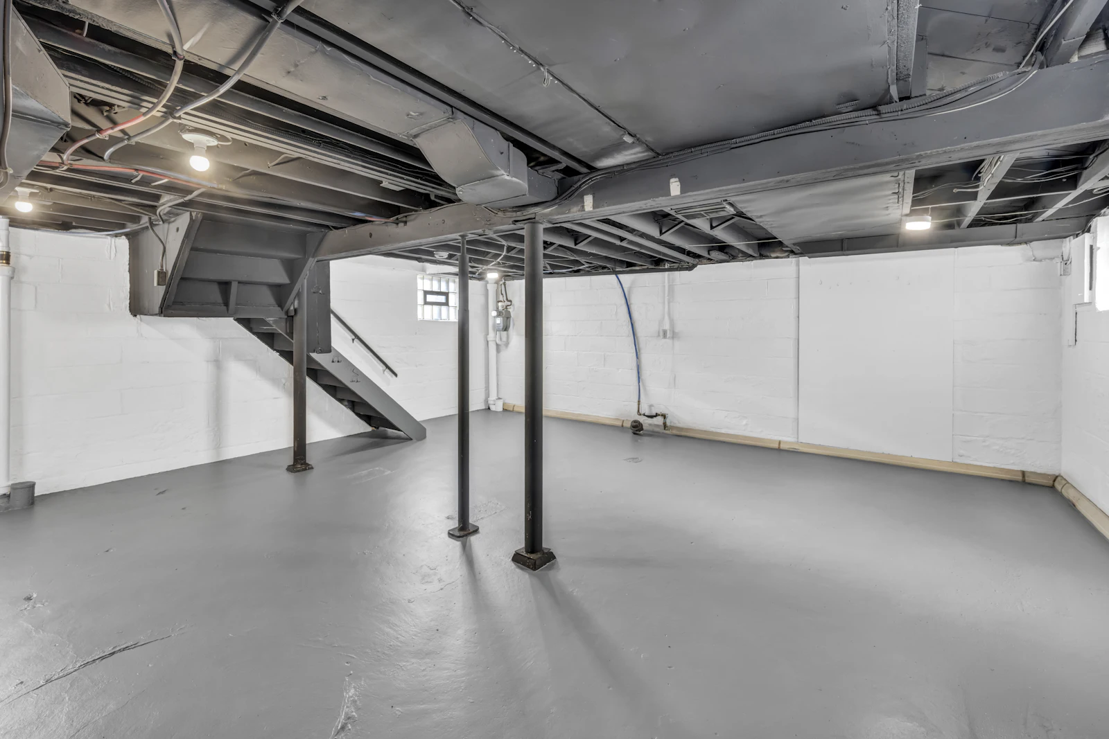 Clean unfinished basement with exposed joists, support posts and stairs