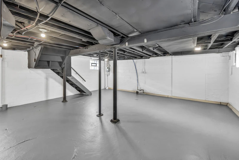A clean unfinished basement with a grey floor and steel posts