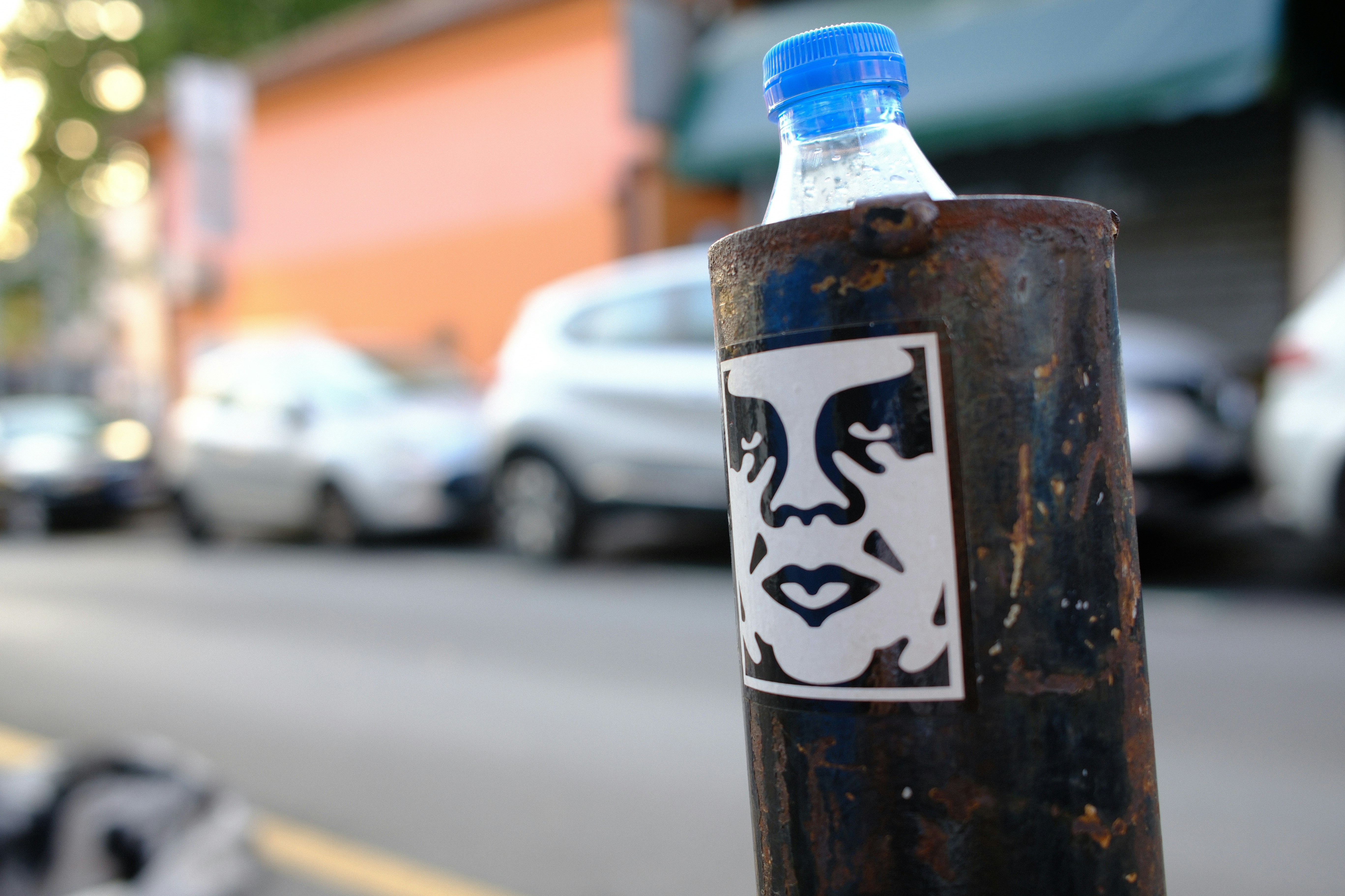 Rusty pole with a sticker, blue bottle, and blurred cars.